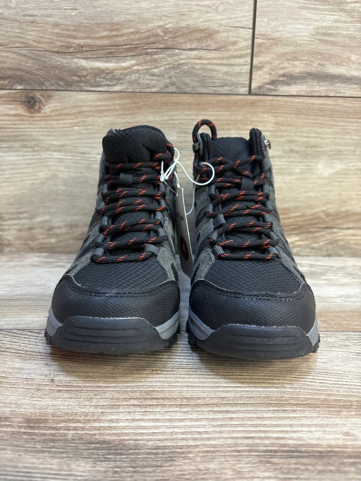 Black and gray kids' high top sneakers with red laces on a wood floor