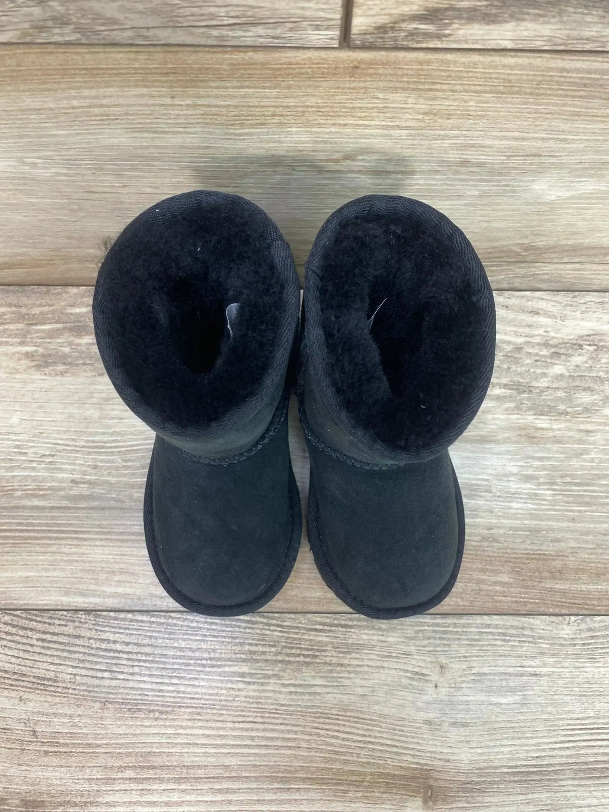 Top view of UGG Toddlers' Classic II boots showing plush black sheepskin lining and suede uppers on light wood floor