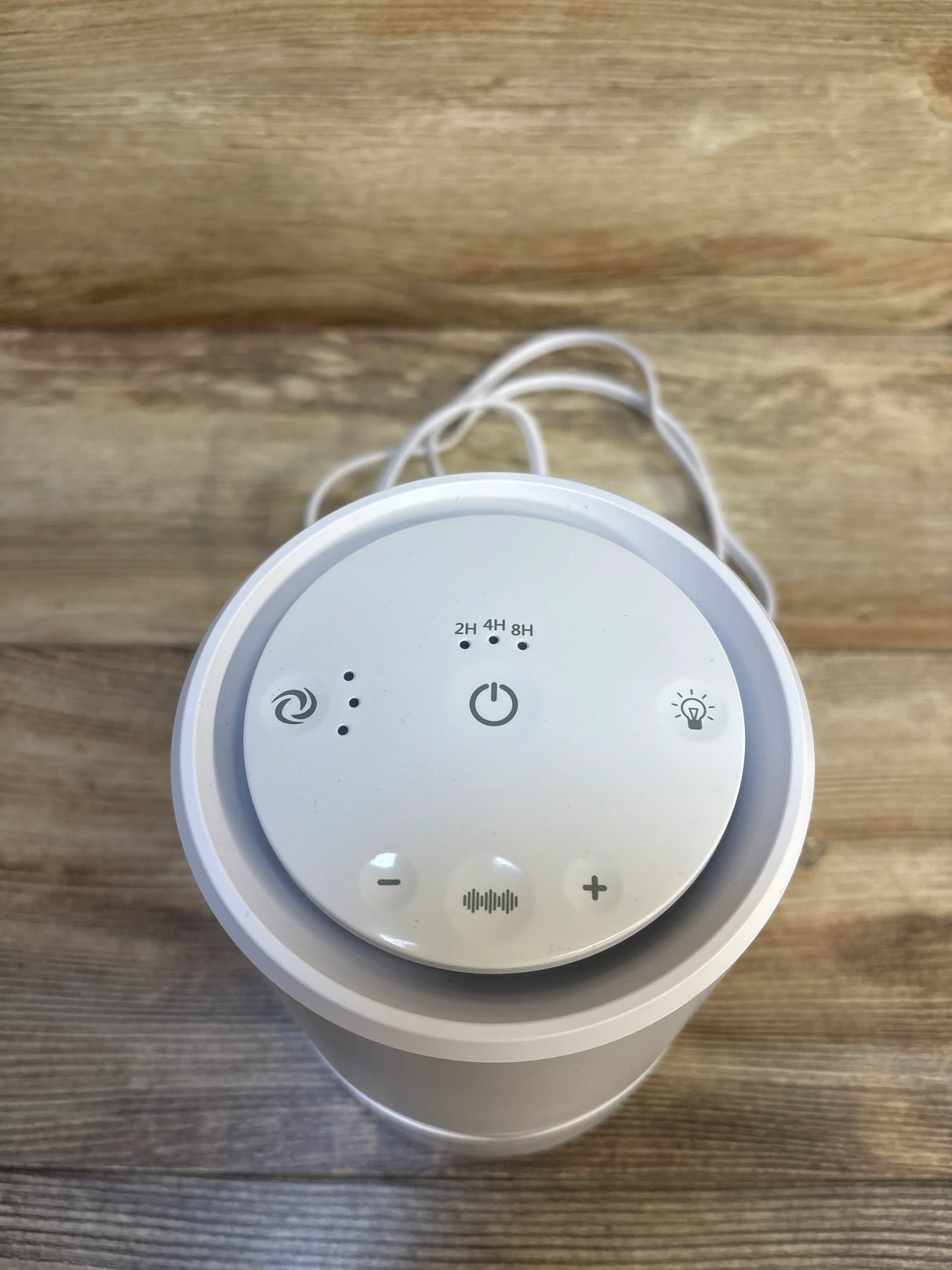 Top view of Frida Baby 3-in-1 air purifier sound machine nightlight showing touch controls and timer 2H 4H 8H on wood surface