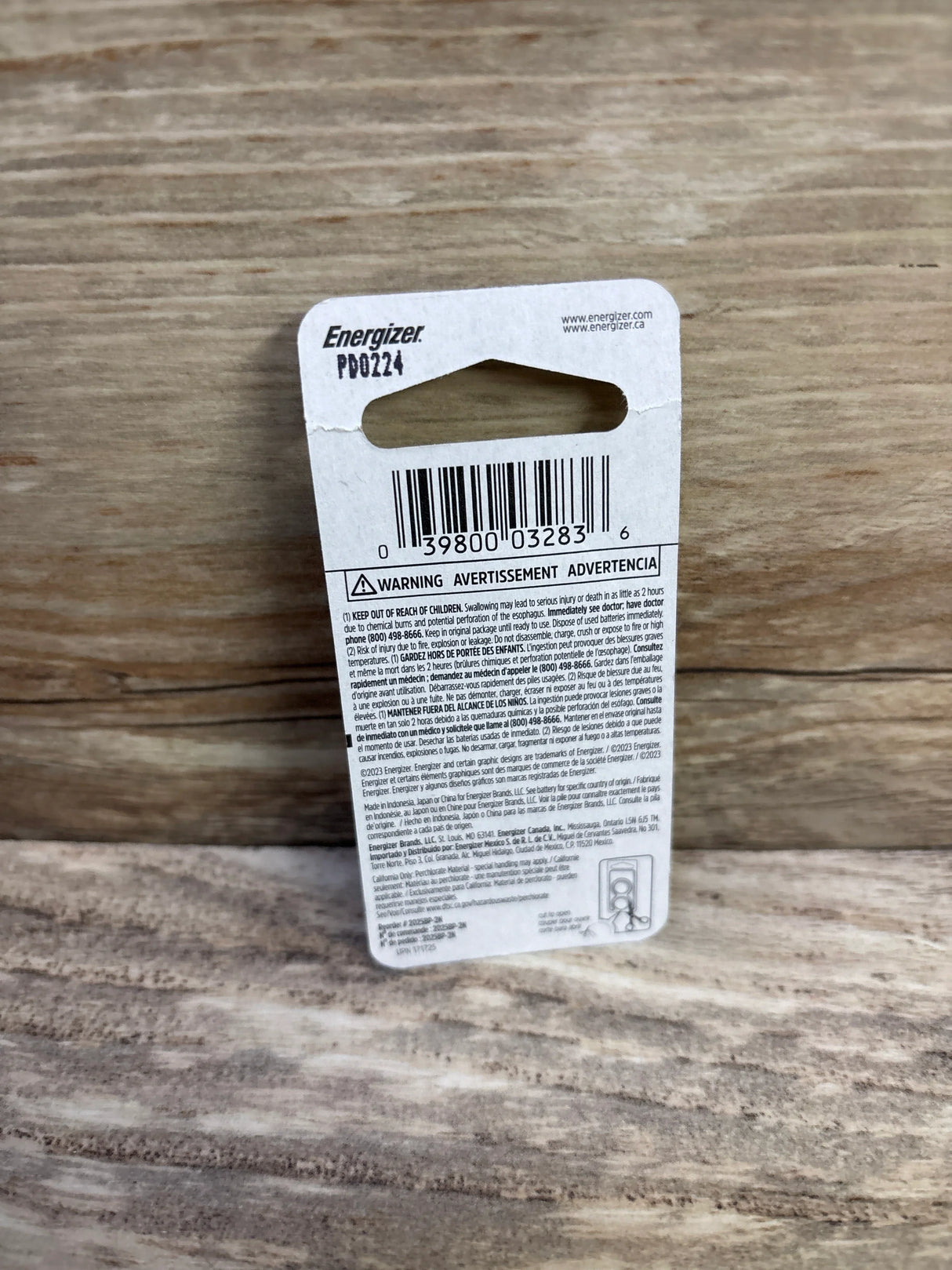 Back view of Energizer 2025 lithium coin battery 2-pack showing barcode and warning text on cardboard backing with wood background