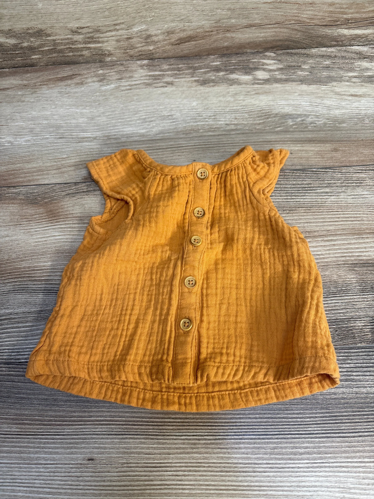 Front view flat lay of Cat and Jack gauze button-up shirt in mustard orange size 3-6m with flutter sleeves on wood plank floor