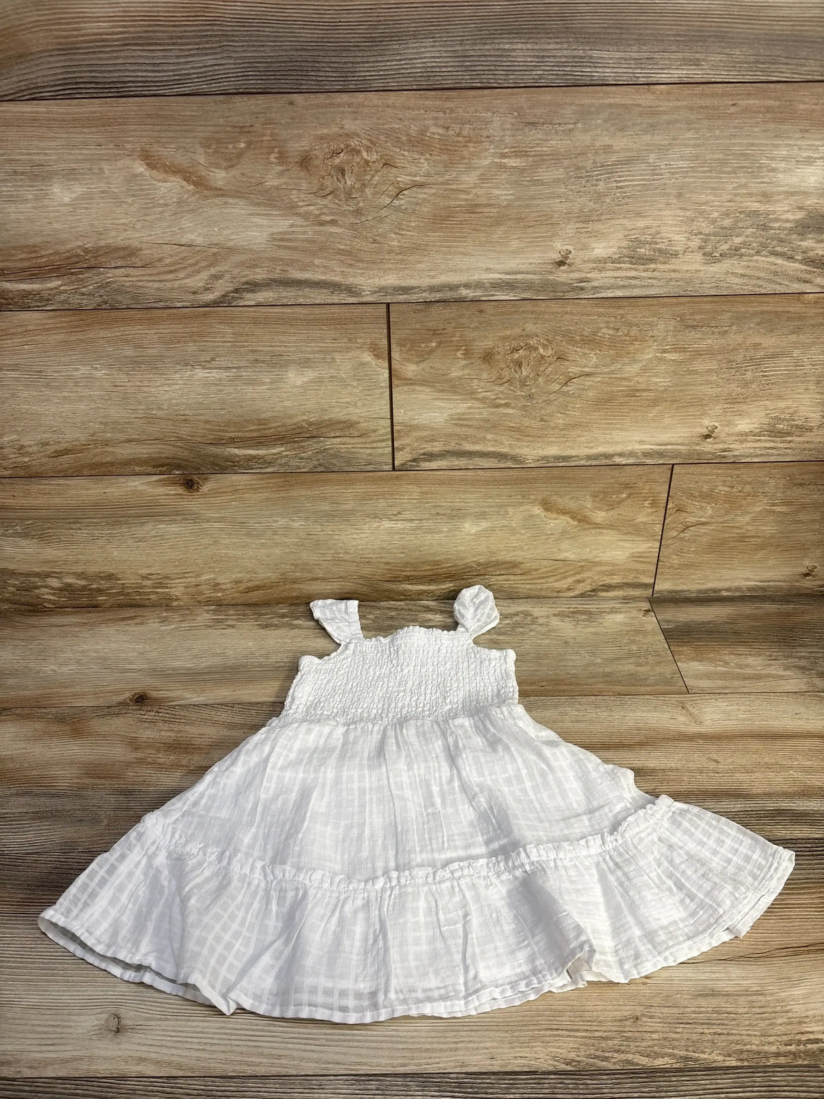 Flat lay of white smocked seersucker sundress (3T) by Janie & Jack showing ruffle straps and tiered skirt on wood background