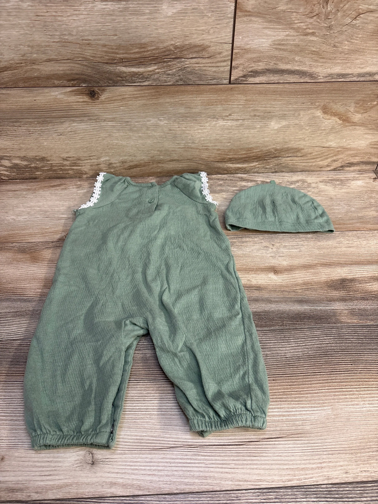 Flat lay of green Daisy Fuentes baby romper and hat with lace shoulder trim and elastic ankle cuffs on wood background
