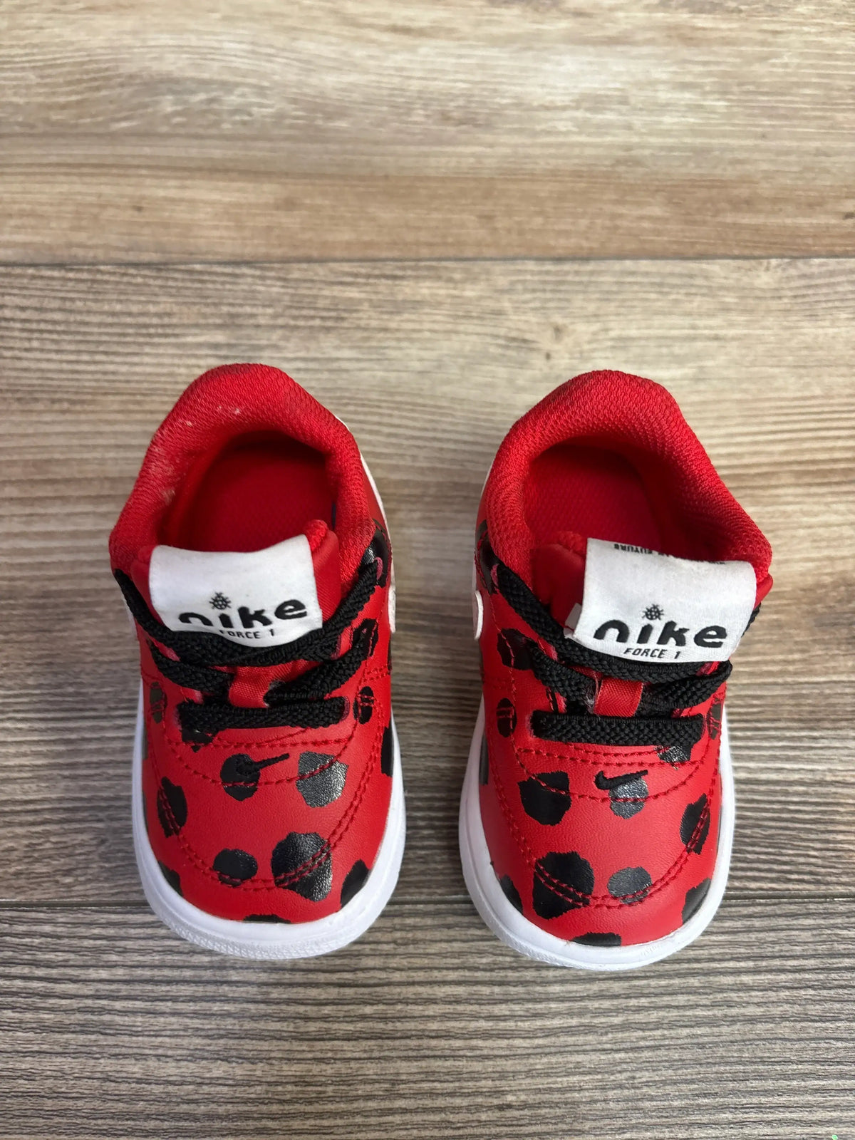 Pair of red Nike Force 1 toddler shoes with black spots and black laces on wooden floor