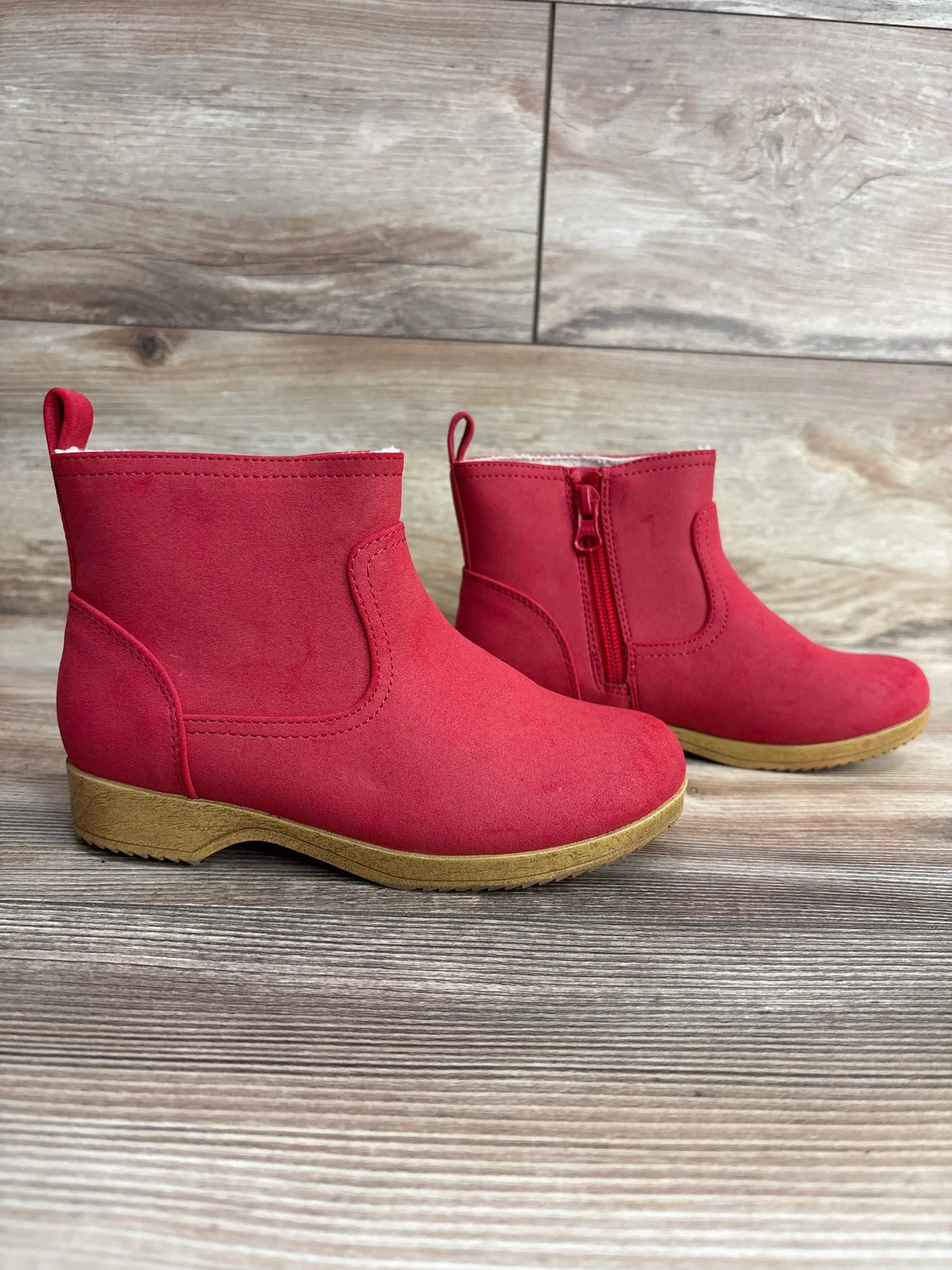 Red toddler ankle boots with side zipper and tan soles on wood floor