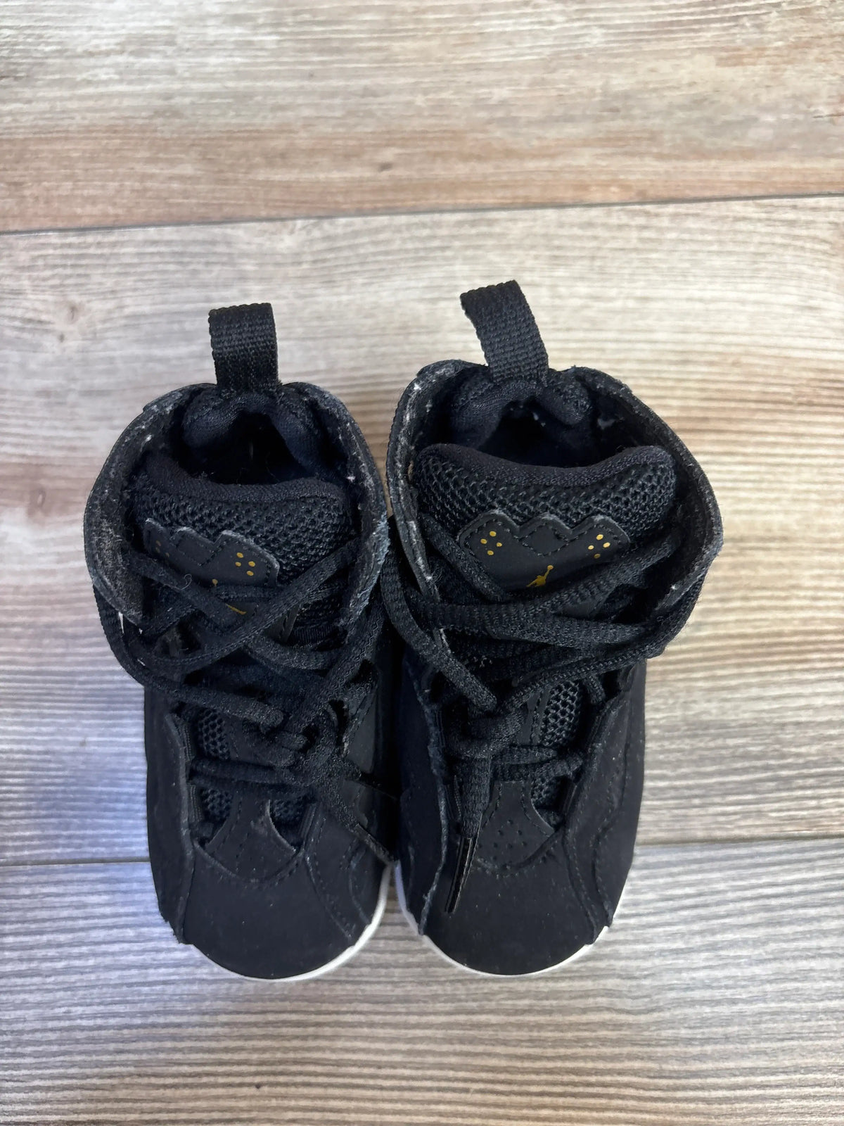 Front view of black Air Jordan True Flight BT kids high-top sneakers showcasing gold Jumpman logos on a wood surface