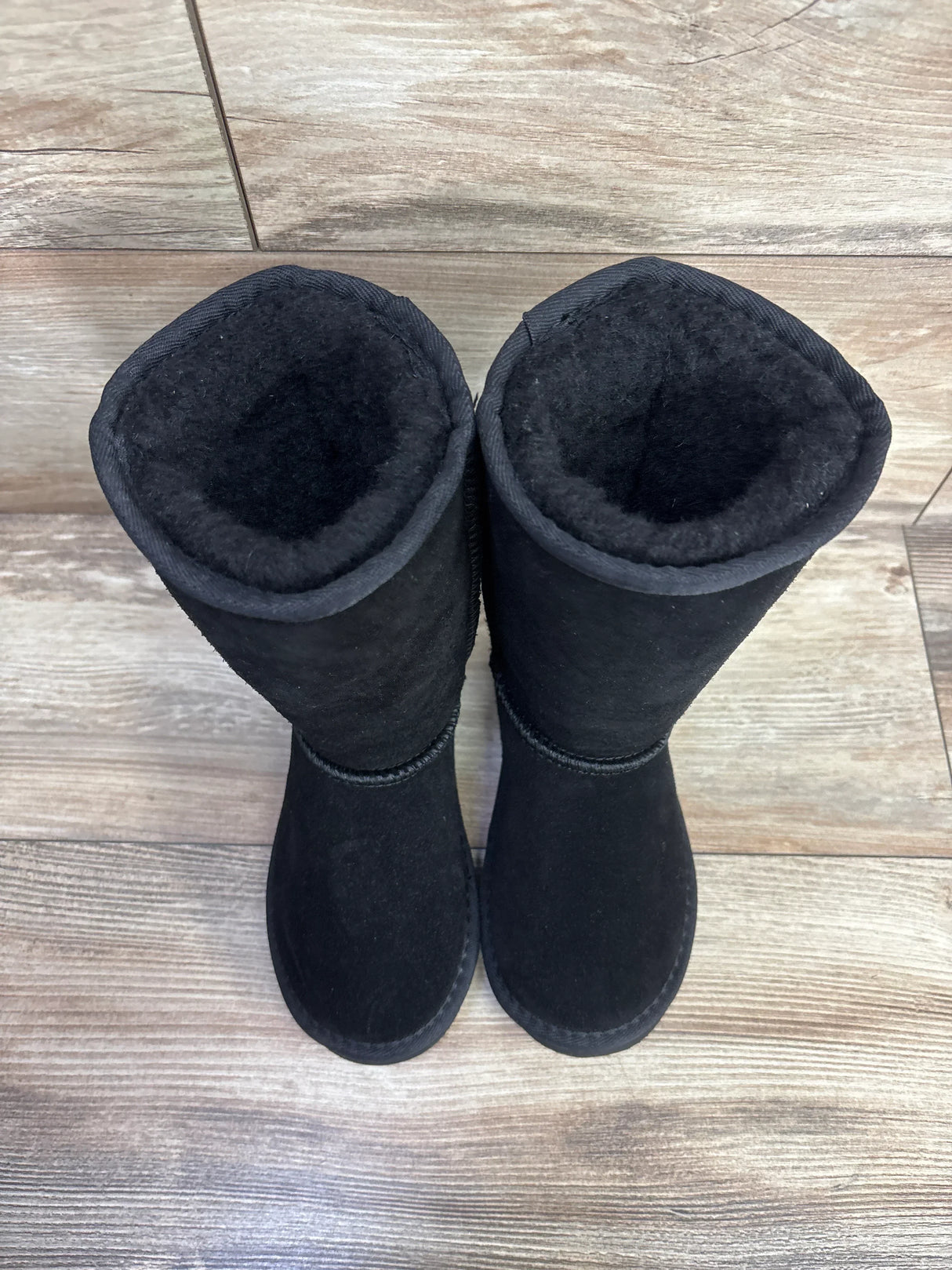 Top-down view of Bearpaw Kenzie tall black wool-lined toddler boots showcasing plush fleece lining and mid-calf shaft on wooden floor