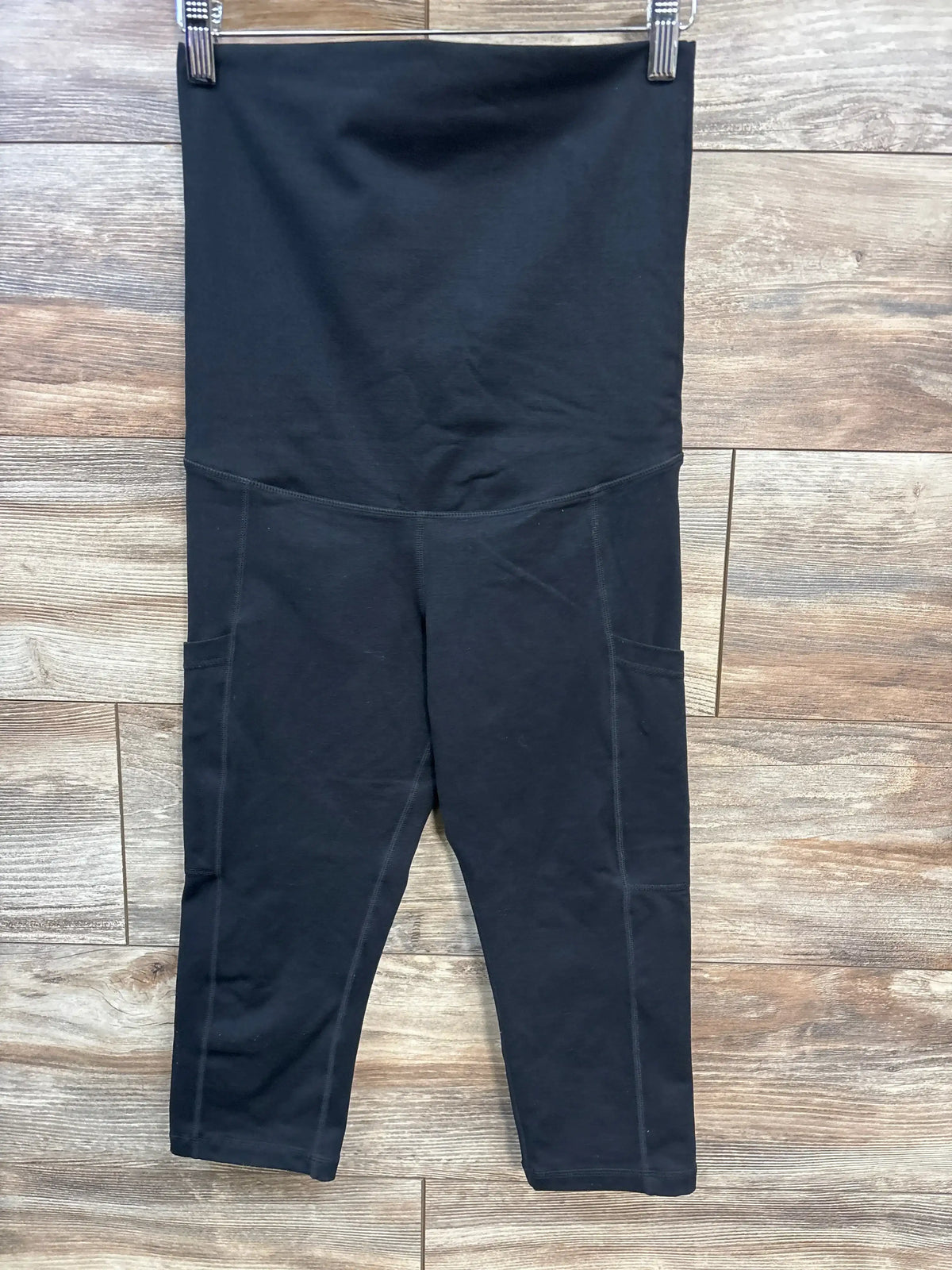 Front view of black Kindred Bravely postpartum leggings with high fold over belly panel and side pockets on wood floor