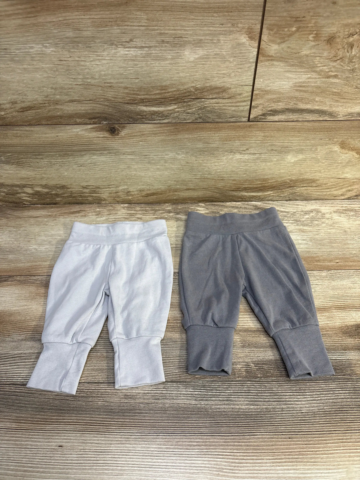 Top-down view of two Hanes baby pants in grey showcasing elastic waistbands and cuffed legs on a wood floor