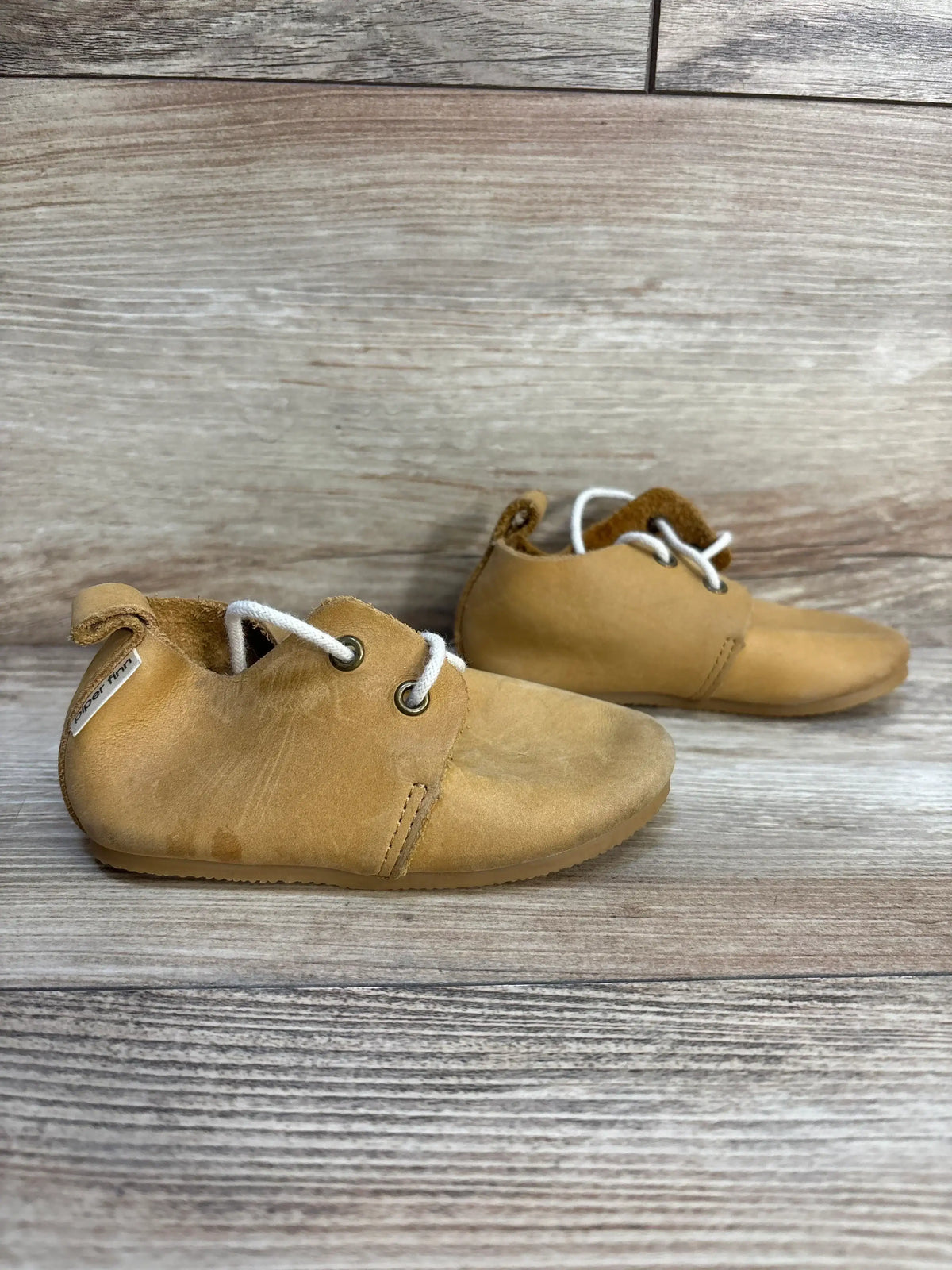 Side view of Piper Finn Natural tan low-top oxfords size 6C showing soft leather upper, white laces and light wear on wooden background