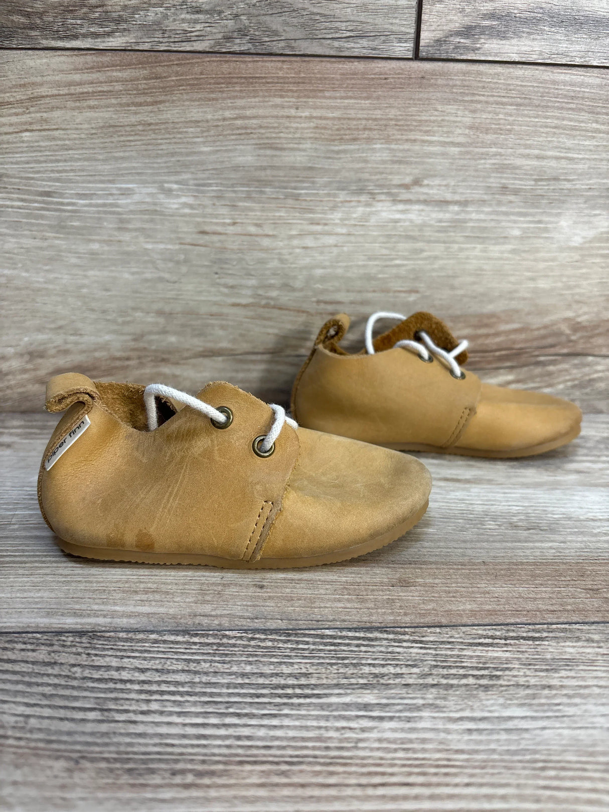 Side view of Piper Finn Natural tan low-top oxfords size 6C showing soft leather upper, white laces and light wear on wooden background