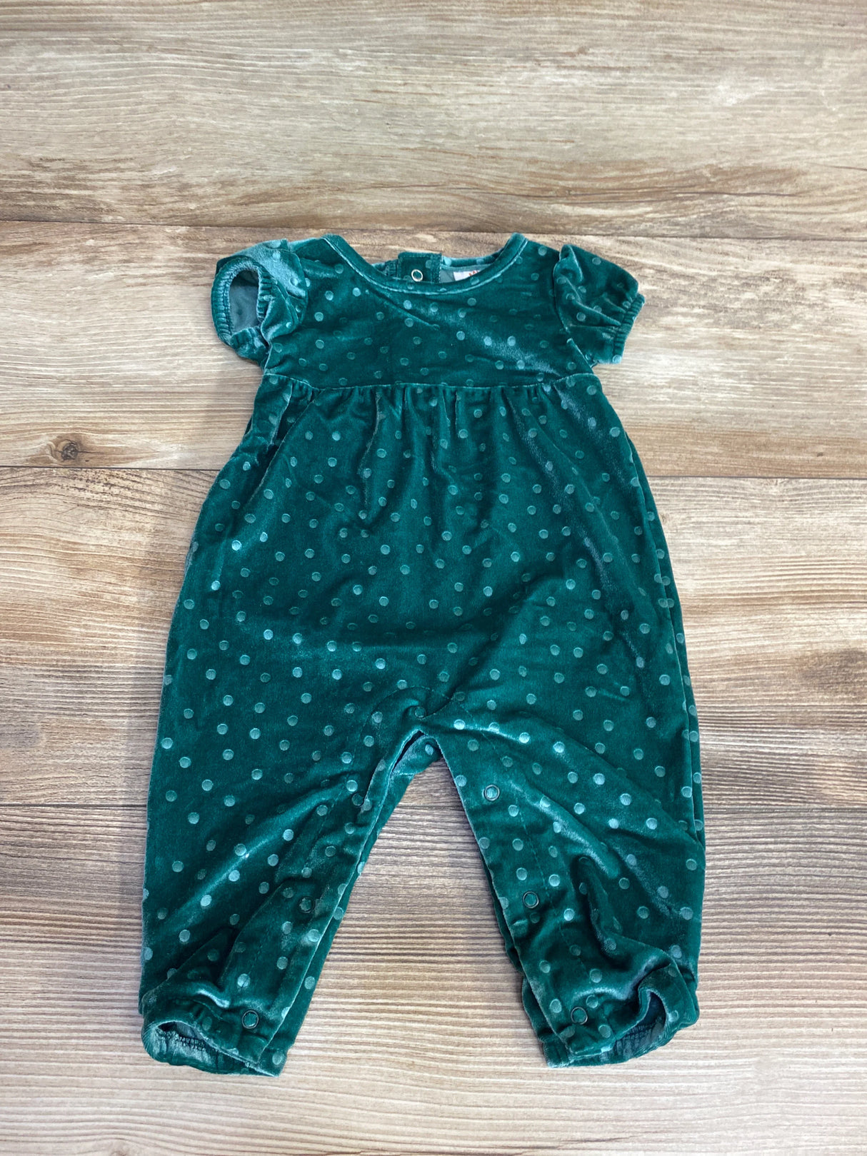 Green velvet baby romper with polka dots, short puff sleeves, and snap closures on wooden background