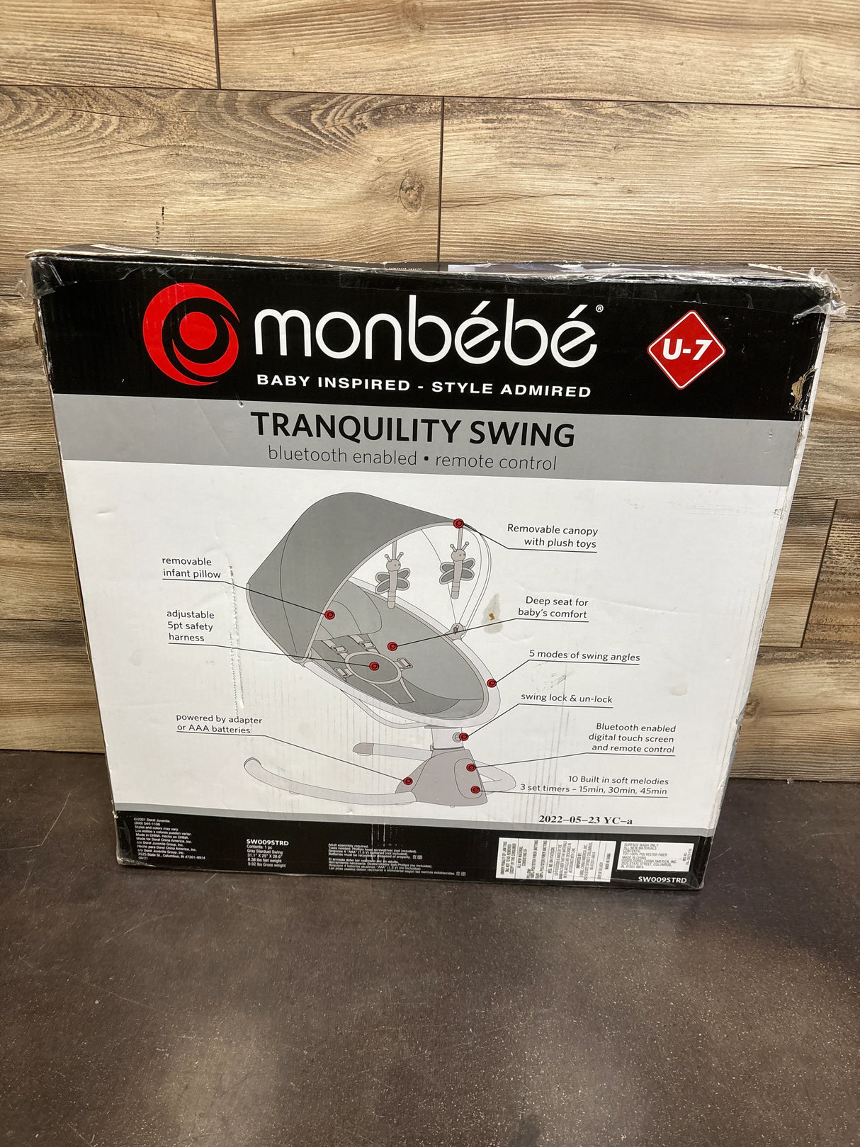 Front of Monbebe Tranquility Swing box showing Bluetooth and remote control features and product diagram on wood floor background