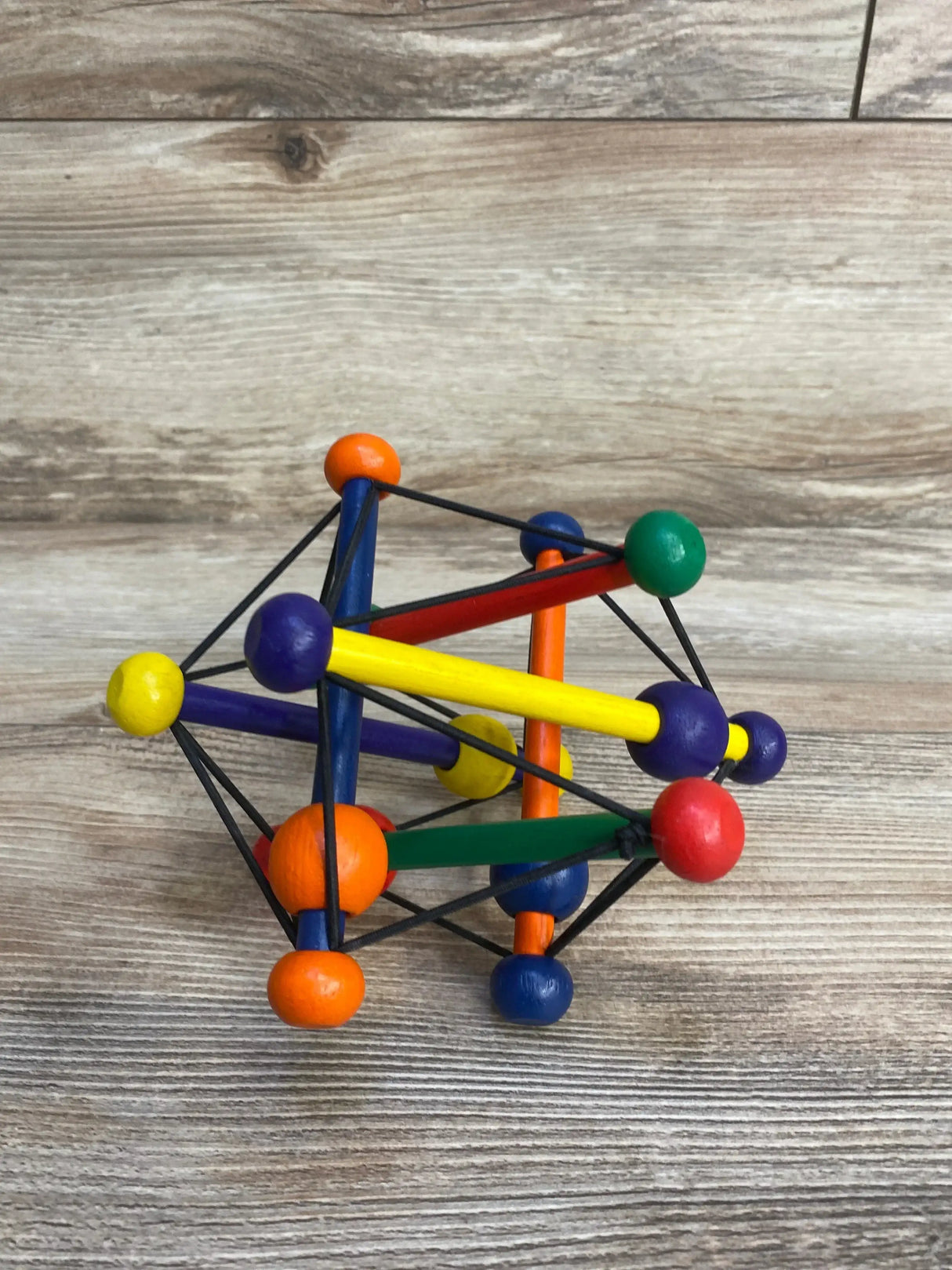 Angled view of Skwish Classic baby toy showing colorful crossed wooden rods and beads on elastic cords on light wood surface