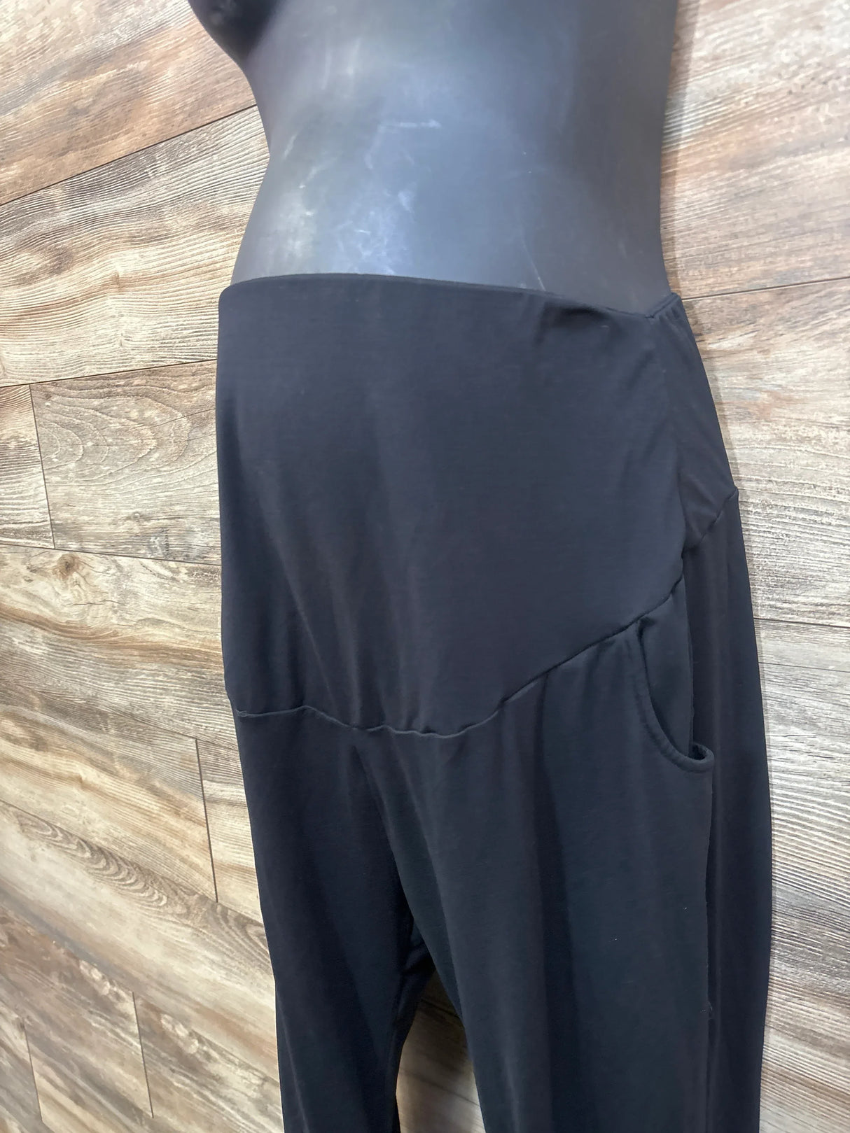 Side view of black maternity leggings showcasing high-rise waistband and side pocket with wood plank background