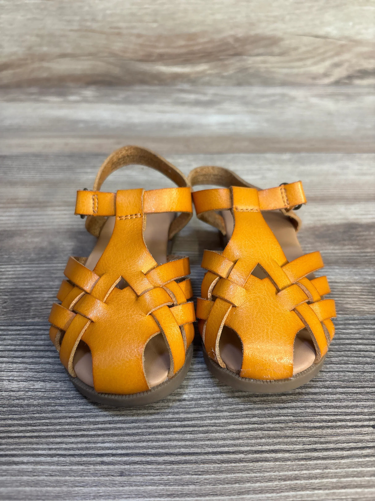 Pair of tan leather toddler sandals with woven straps on a wood background