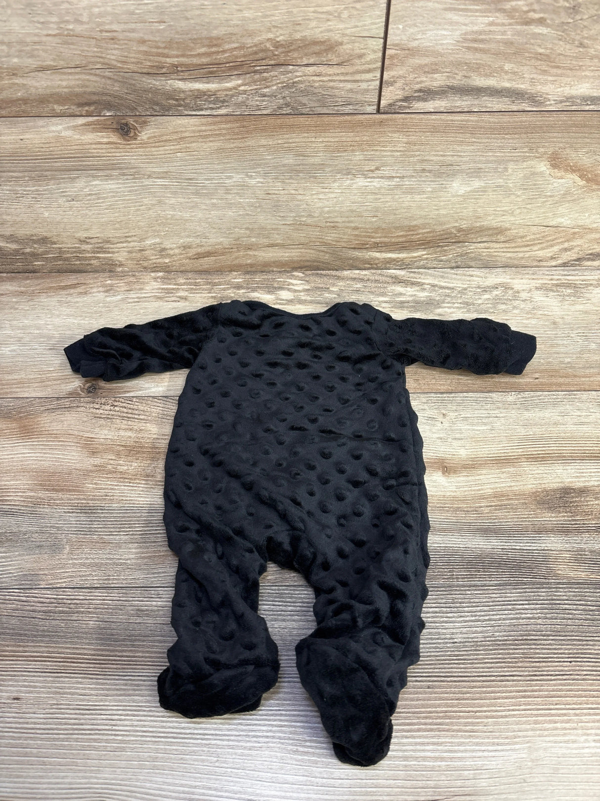 Black textured baby sleeper pajamas on wood floor, soft plush footed onesie.