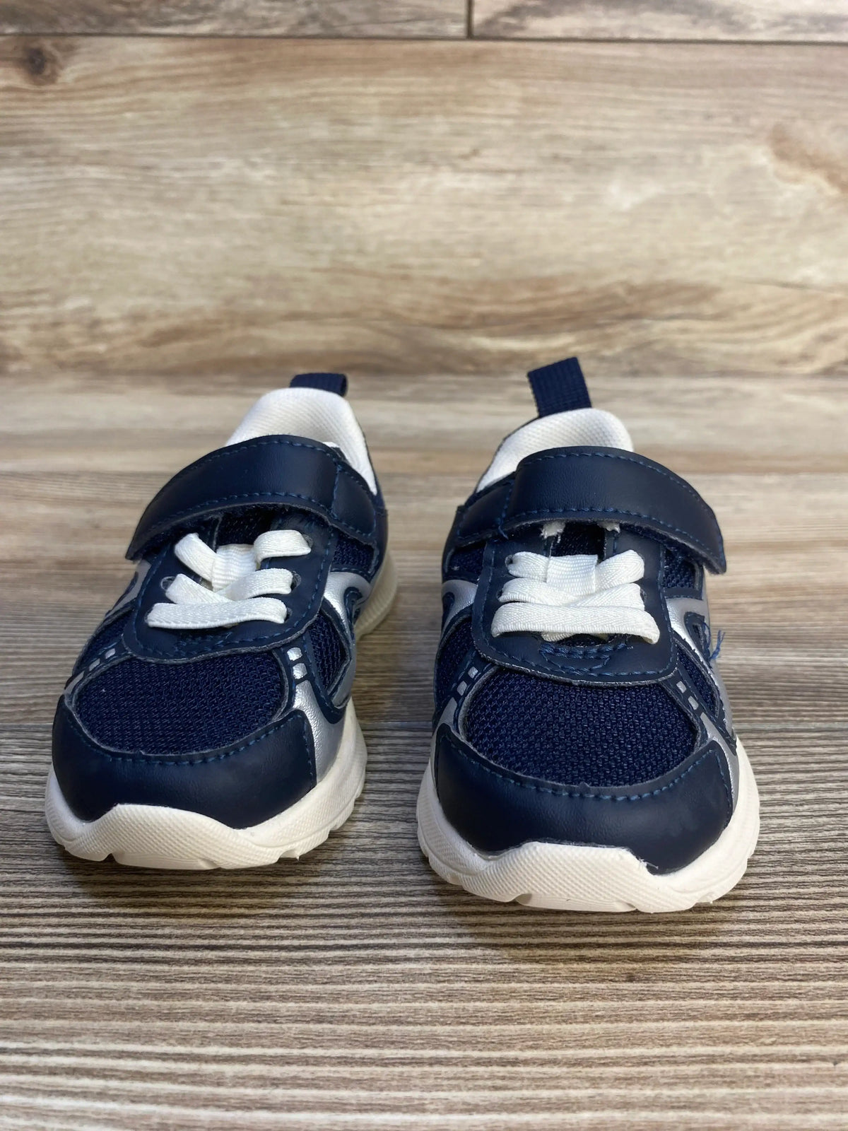 Navy blue and white toddler sneakers with velcro straps on wood background