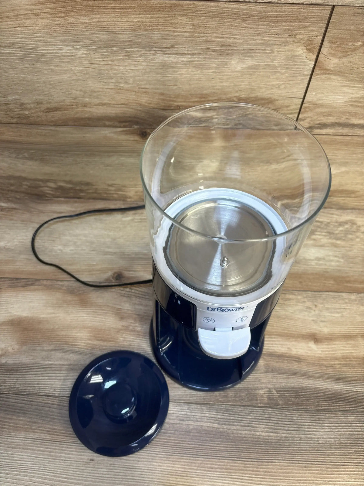 Top-down view of Dr. Brown’s Insta-Prep dispenser with clear tank, white dispense button and detached navy lid on wood background