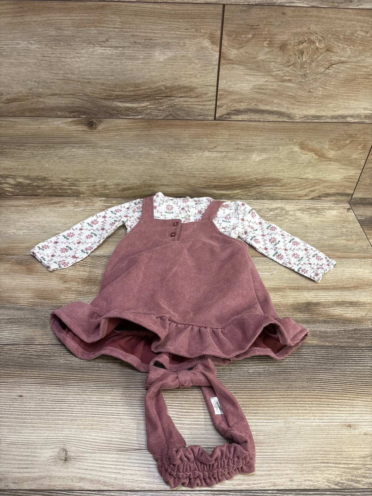 Front view of Daisy Fuentes 3-piece skirtall set with floral long-sleeve bodysuit and matching headband on wood background