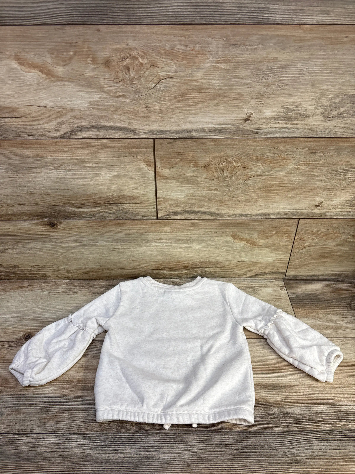 Flat view of Kids Headquarters ivory unicorn pullover sweatshirt showcasing long sleeves and ribbed cuffs with a wood background