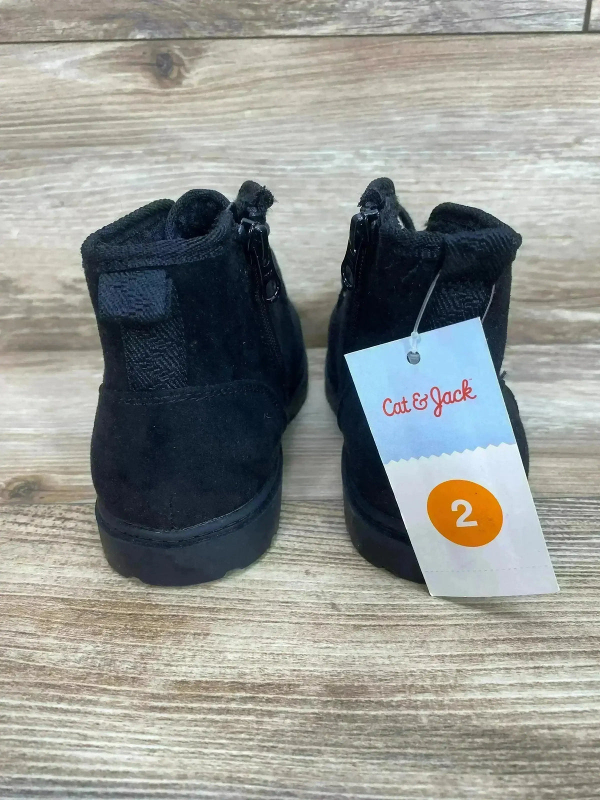 Rear view of Cat and Jack kids' Ronin boots in black showing back zipper, heel pull tab, and size tag 2 on a wood background