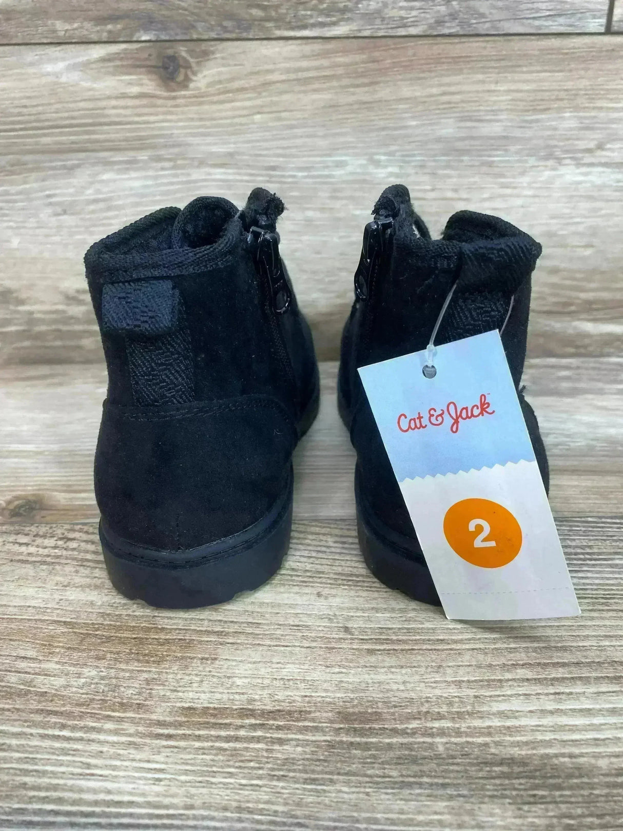 Rear view of Cat and Jack kids' Ronin boots in black showing back zipper, heel pull tab, and size tag 2 on a wood background