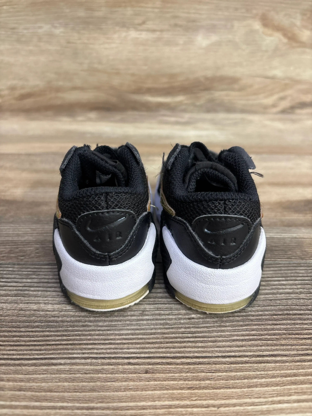 Back view of Nike Air Max Excee TD sneakers in black showcasing Air branding heel white midsole and gold air unit on wood plank floor