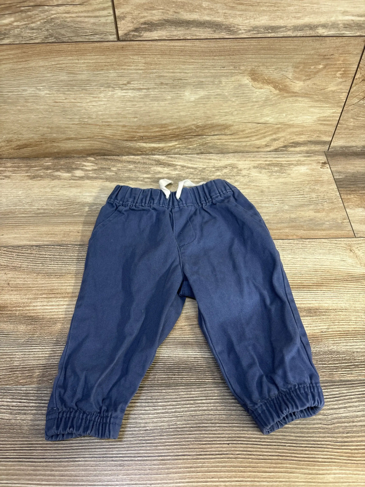 Front view of blue baby drawstring joggers size 6 months showcasing elastic waistband with white drawstring and elastic cuffs on wood floor background