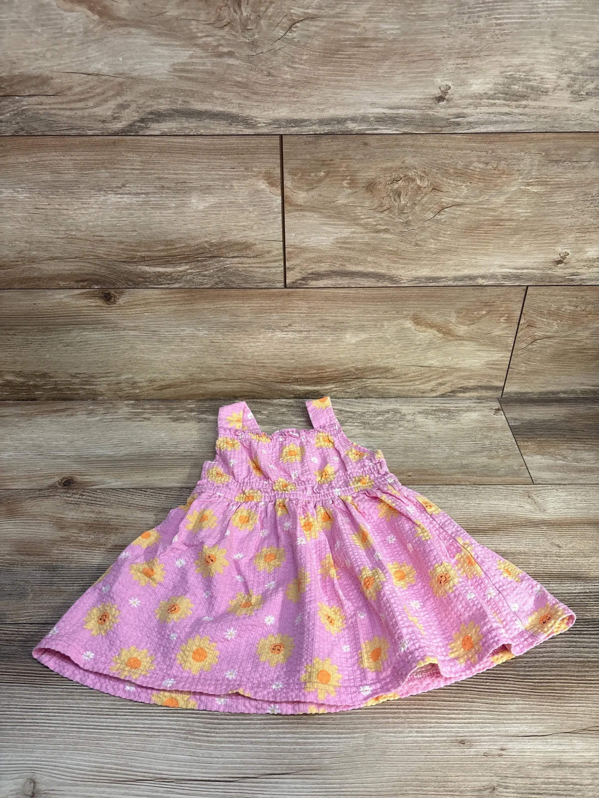 Front view of Little Lass textured pink dress showcasing floral pattern and gathered waist on a wood-grain background