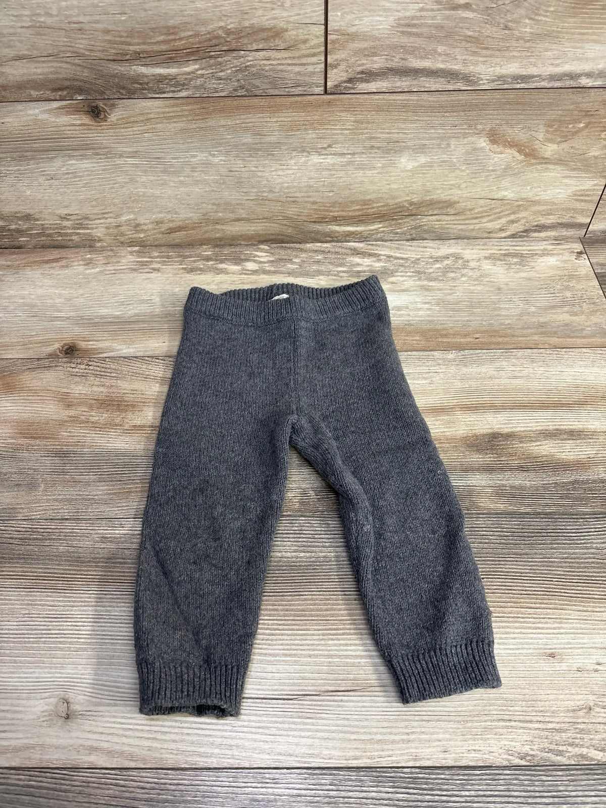 Gray knit baby pants laid flat on a wooden surface, soft warm fabric for toddlers