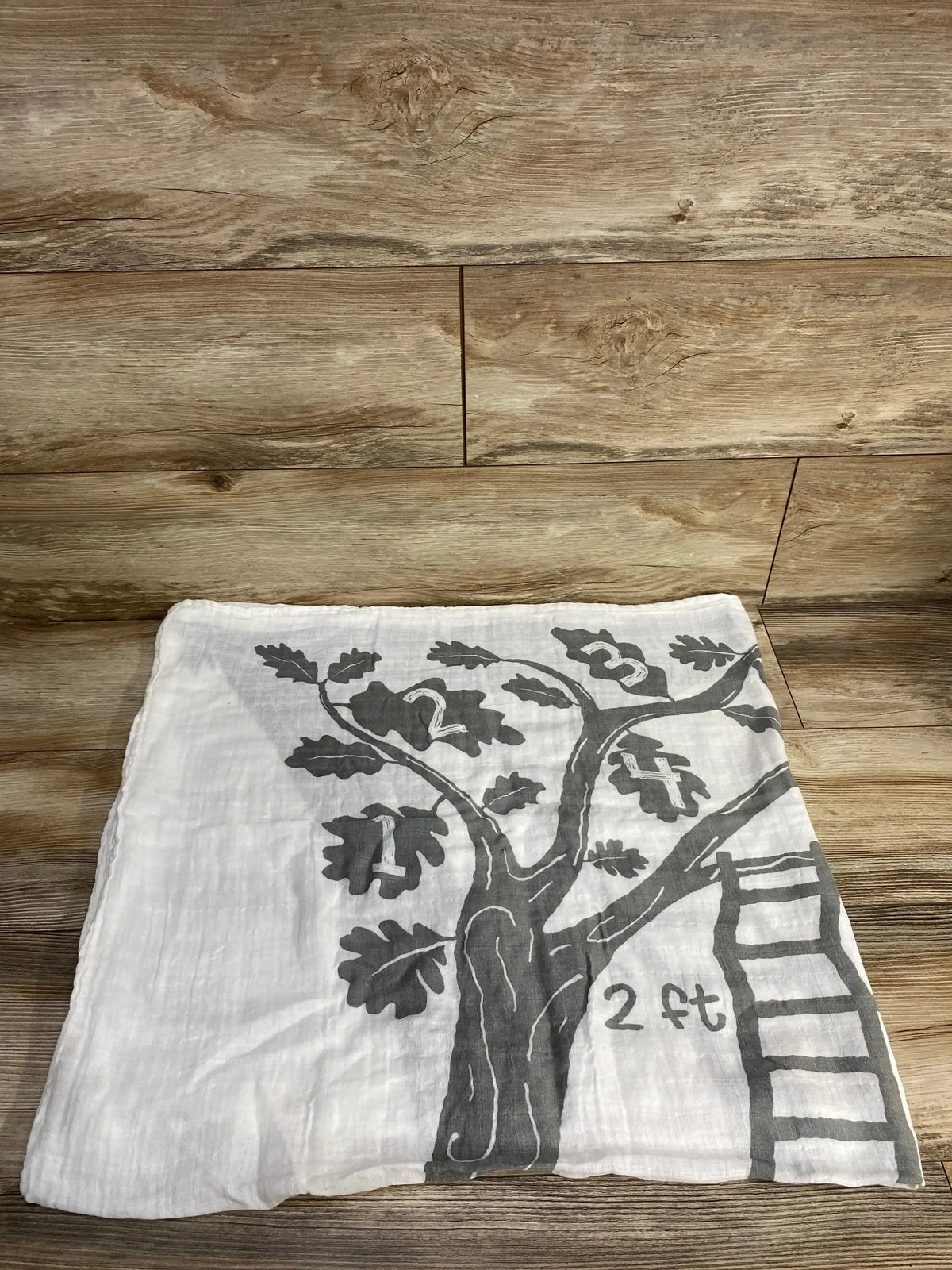 Flat lay of Baby Wings height milestone blanket (tree) showing gray tree print, numbered leaves 1-4, ladder scale, 2 ft mark