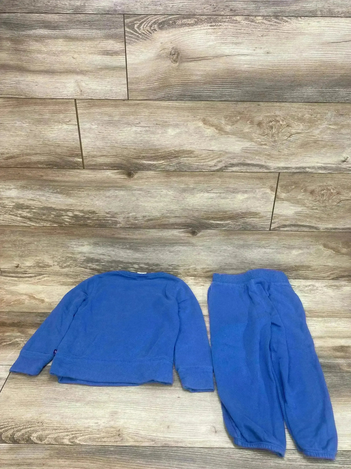 Flat lay of Gap Kids blue 2-piece sweatshirt and joggers showing crewneck sweatshirt and elastic waist joggers on wood floor background