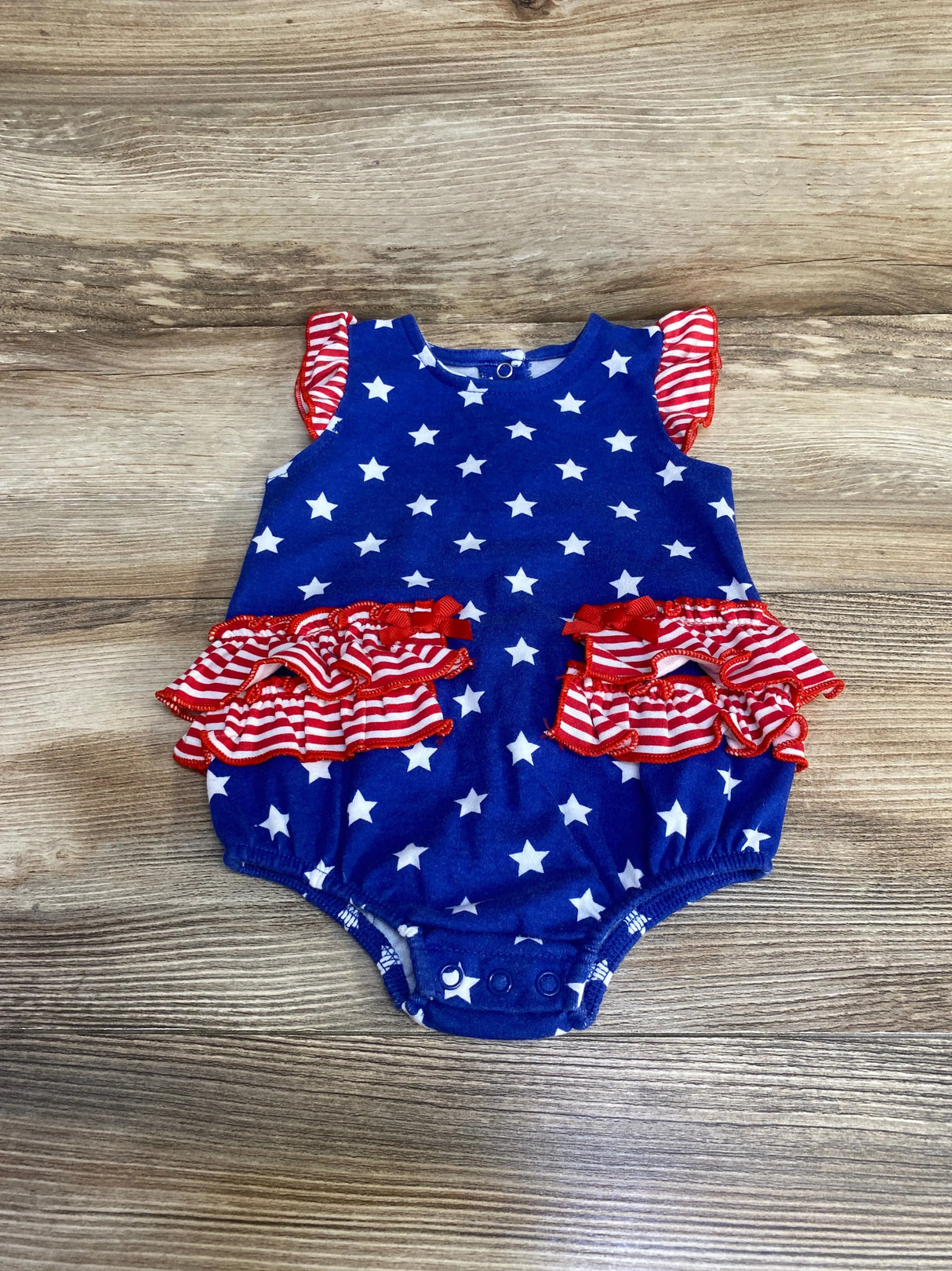 Top-down view of Baby Starters blue 9m romper with white stars and red-striped ruffle details on wood background