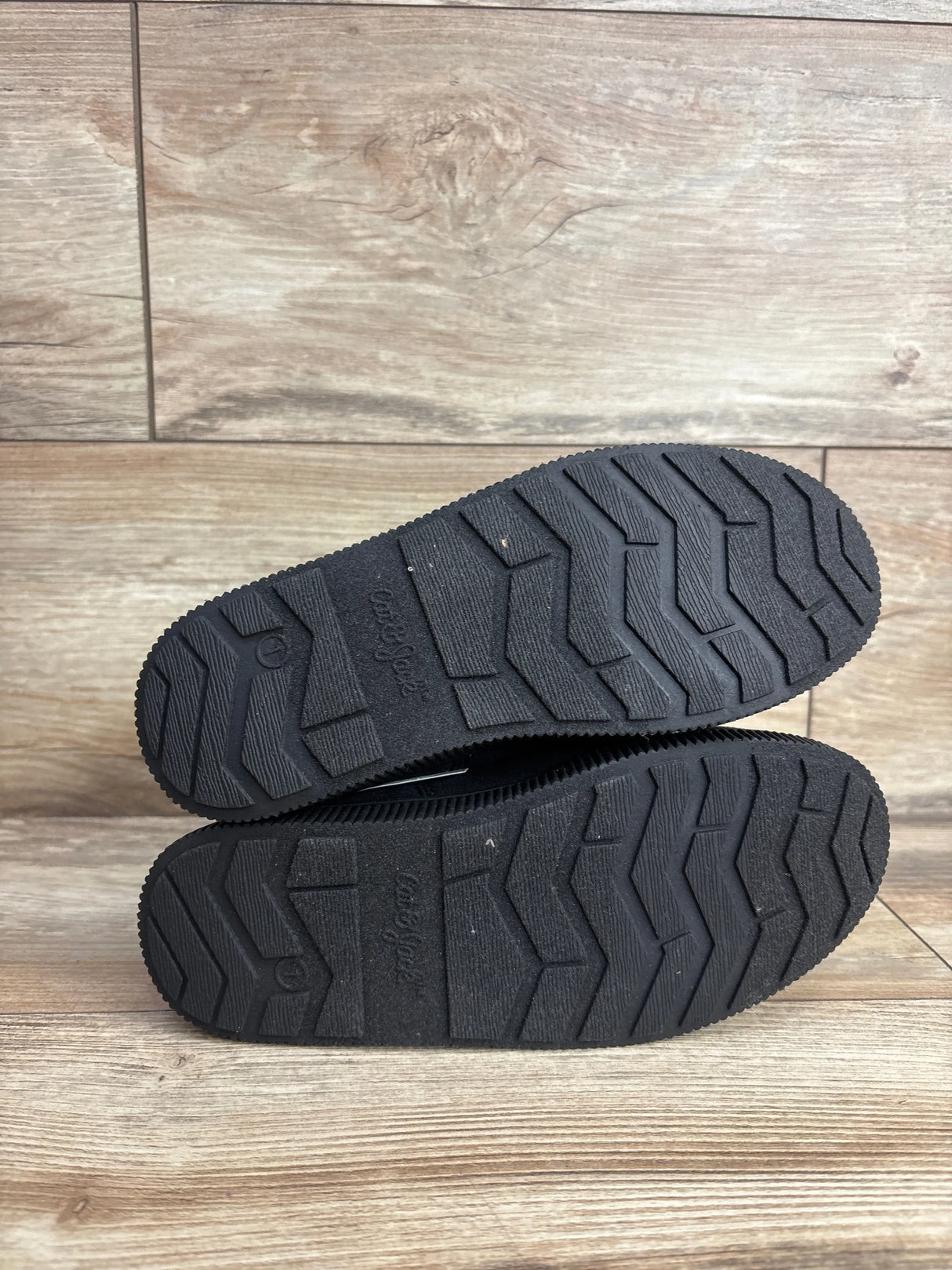 Black rubber soles of kids' shoes with textured tread pattern on wooden floor