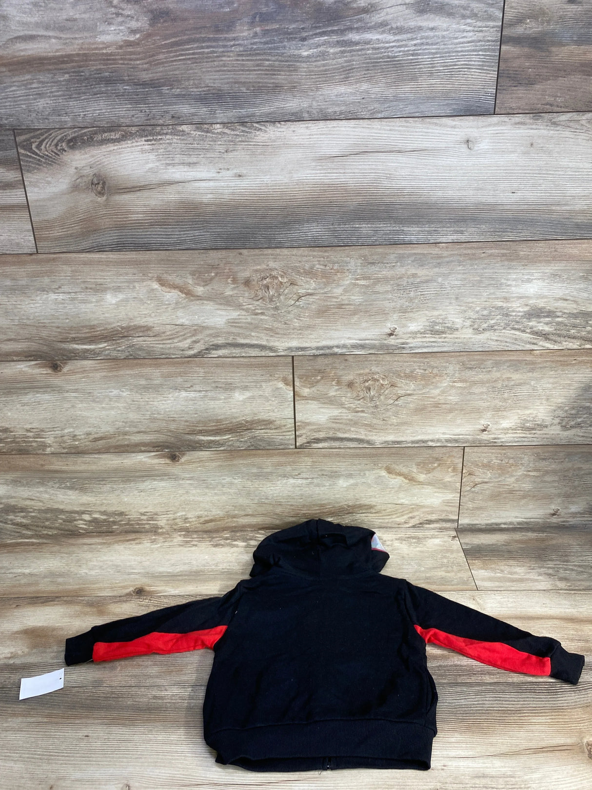 Black kids hoodie with red sleeve stripes laid flat on wood background