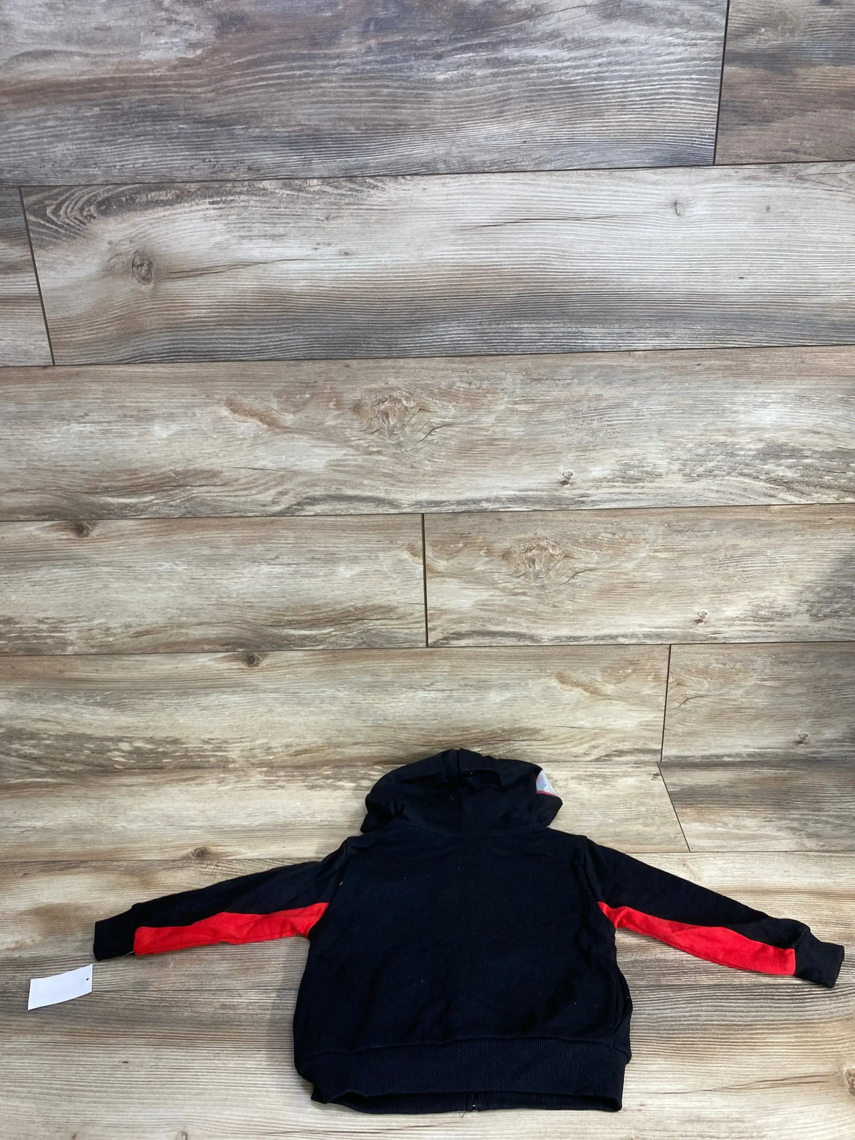 Black kids hoodie with red sleeve stripes laid flat on wood background