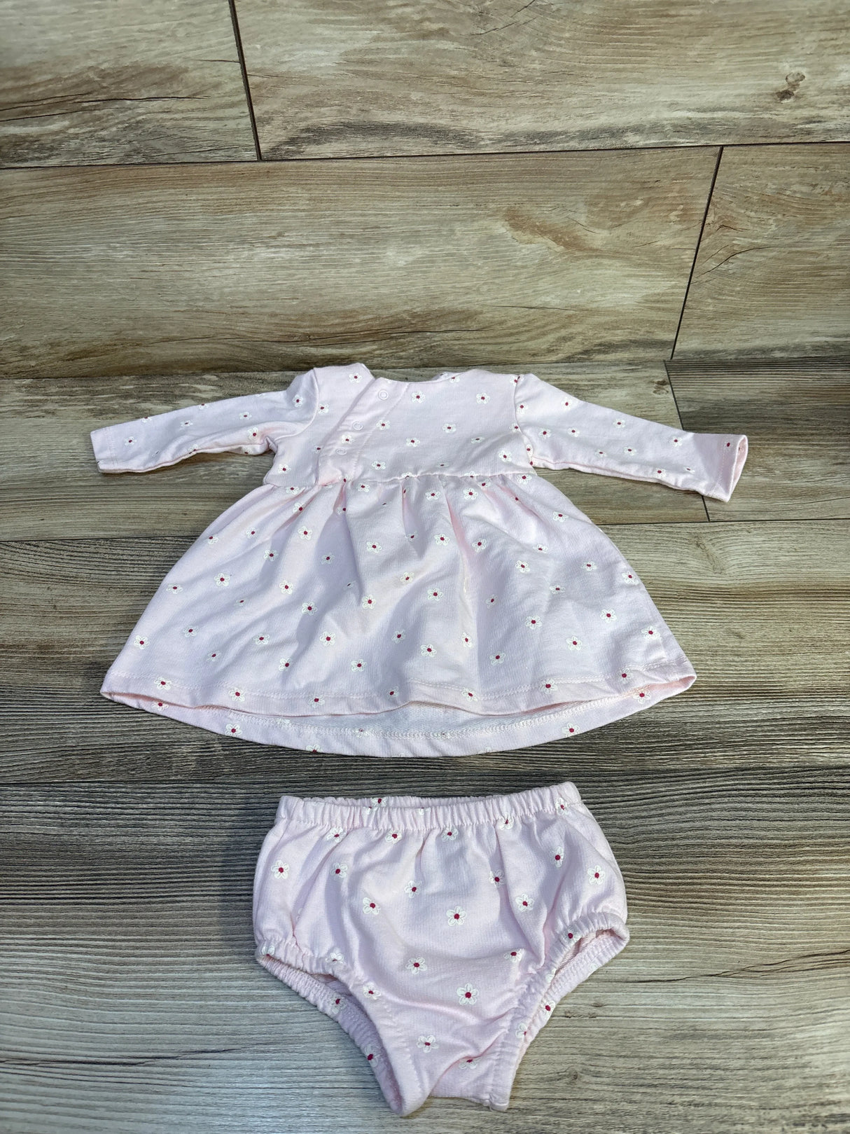 Light pink long sleeve baby dress and matching bloomers with small daisy print on wood floor