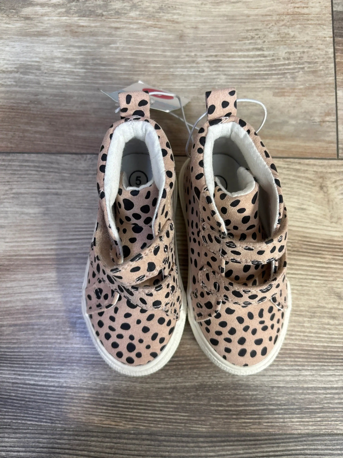 Top view of toddler high-top sneakers in beige leopard print with double Velcro straps and white rubber soles on wood floor