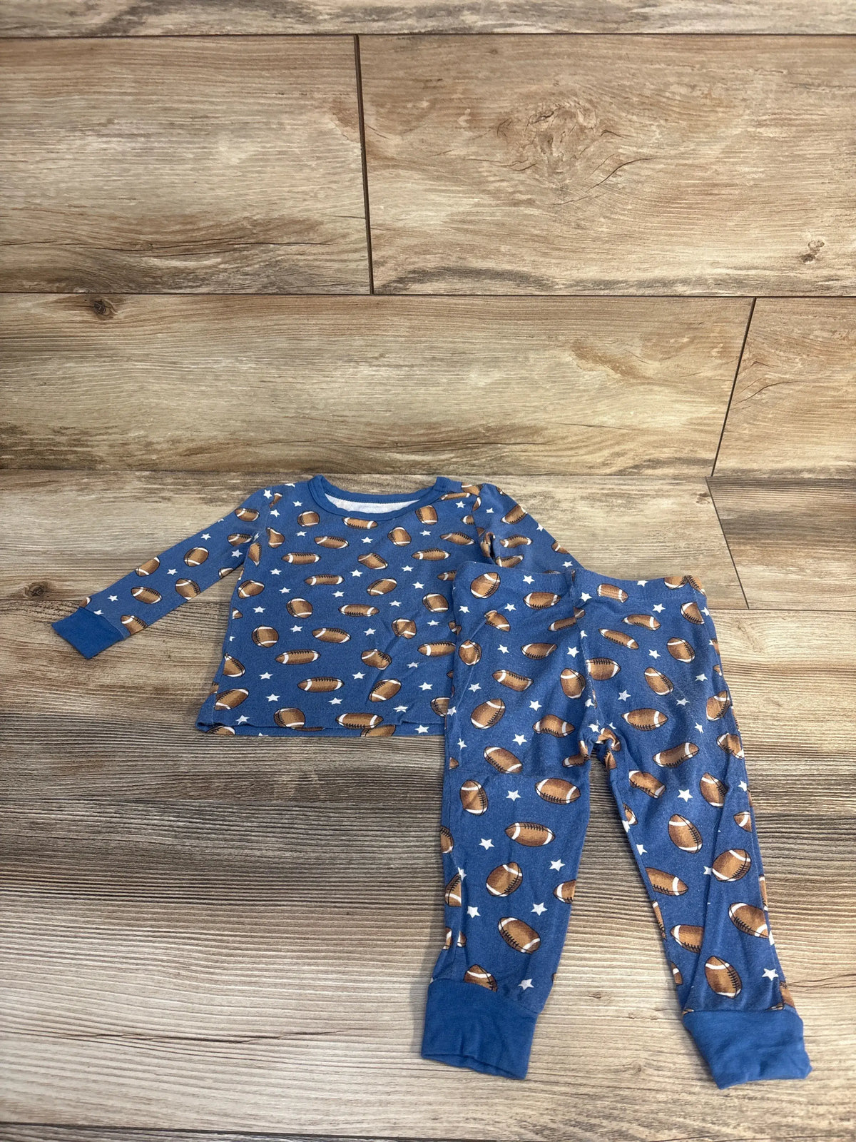 Top view of Little Me two-piece bamboo pajama set showcasing blue football and star print with wood-look background