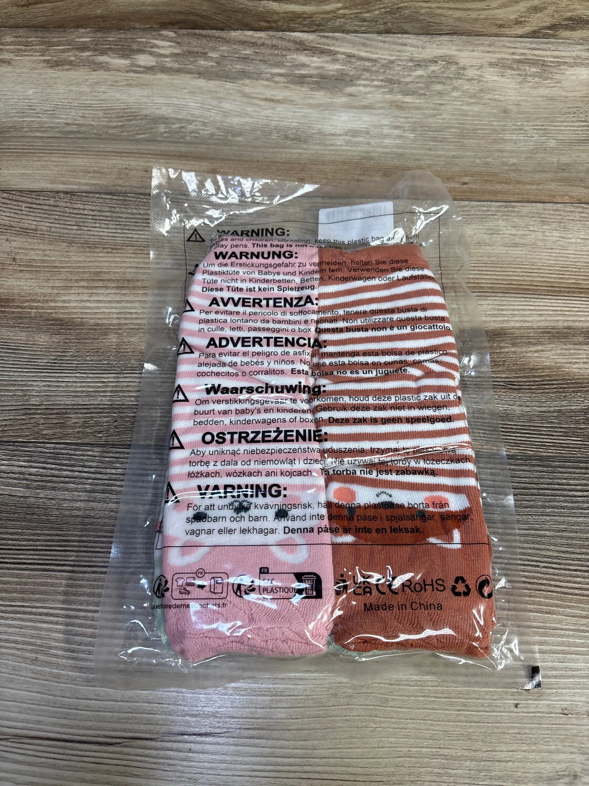 Front view of three pack toddler leg warmers in pink and peach stripes, sealed in clear plastic