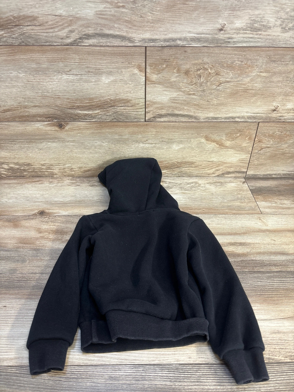 Black kids hooded sweatshirt with ribbed cuffs laid flat on wood floor