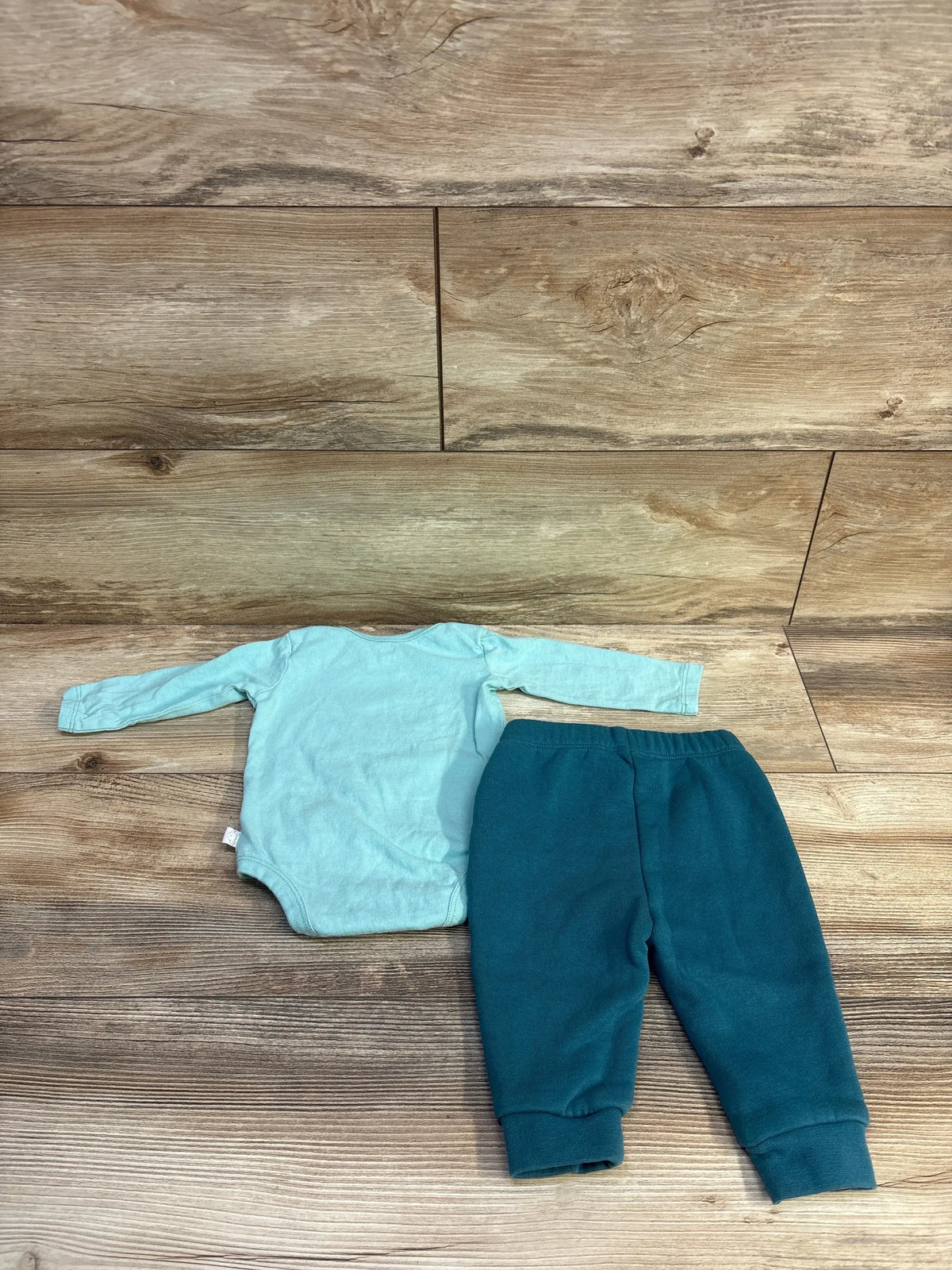 Top-down view of Koala Kids 2pc bodysuit and pants set showcasing a light blue bodysuit and dark blue pants on a wood surface