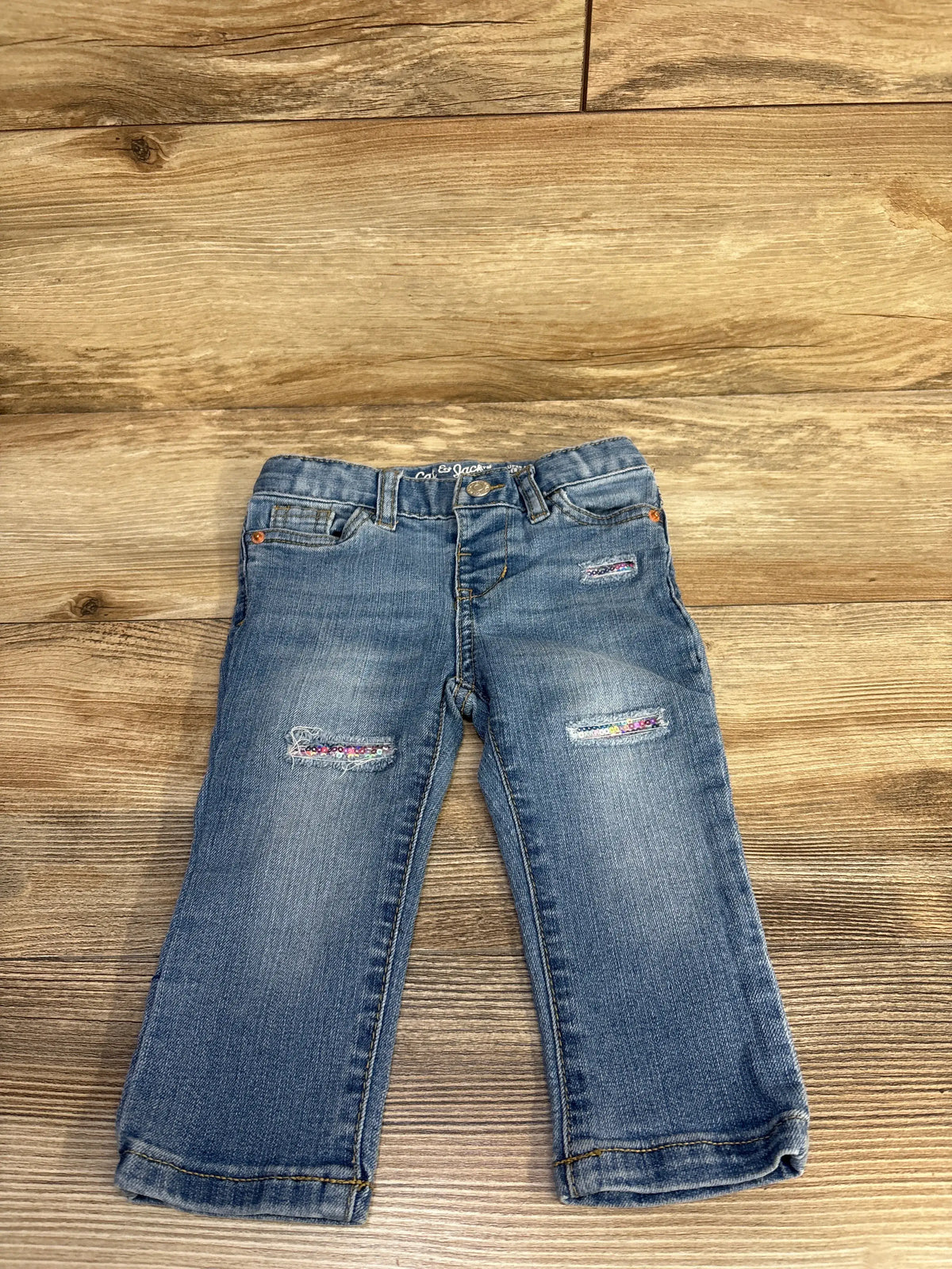 Front view of Cat & Jack skinny distressed sequin jeans showcasing blue denim and sequin patches on wood-grain background