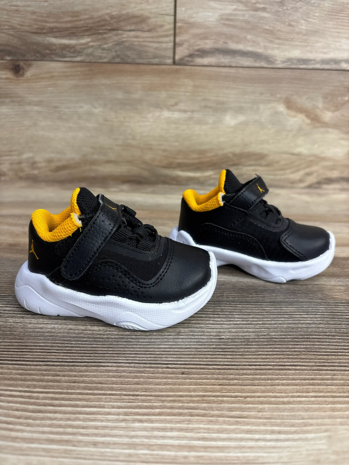 Black toddler sneakers with yellow lining and white soles on wooden background