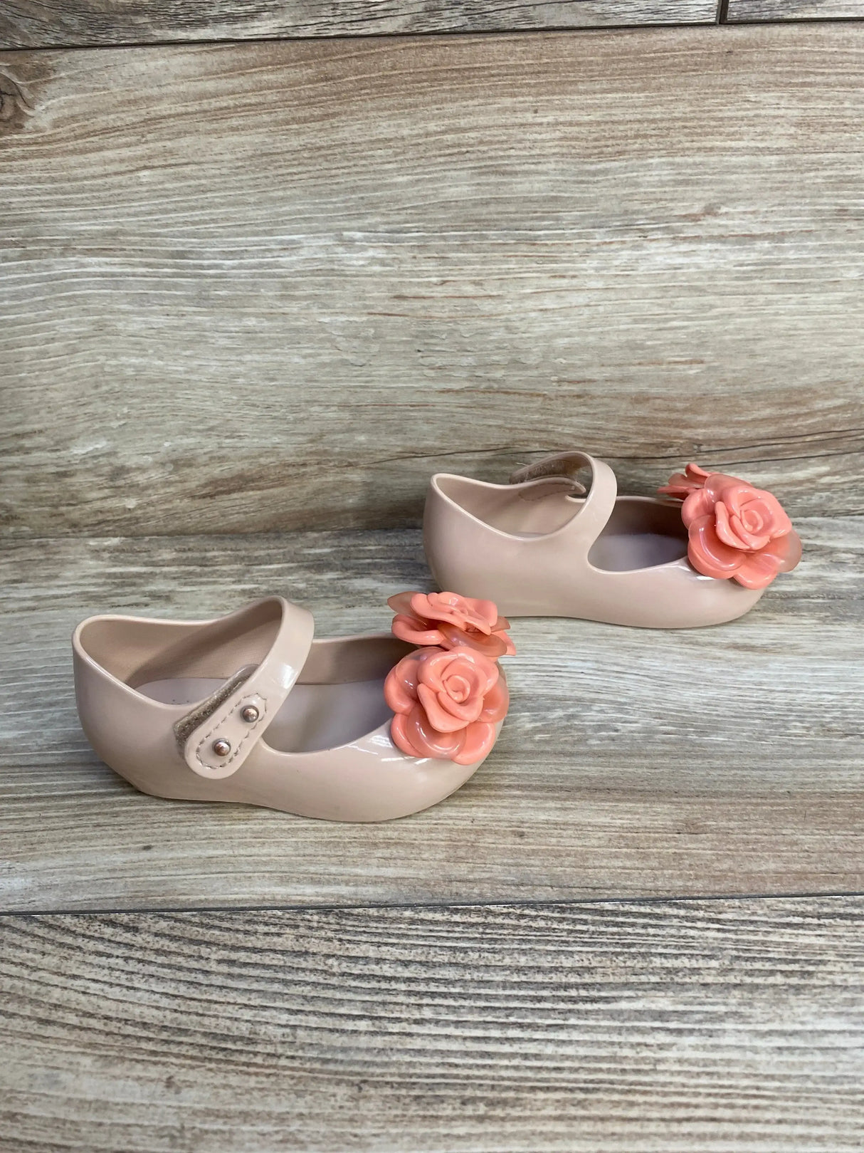Three-quarter view of Mini Melissa Ultragirl flats in beige and pink with flower detail and glossy jelly finish