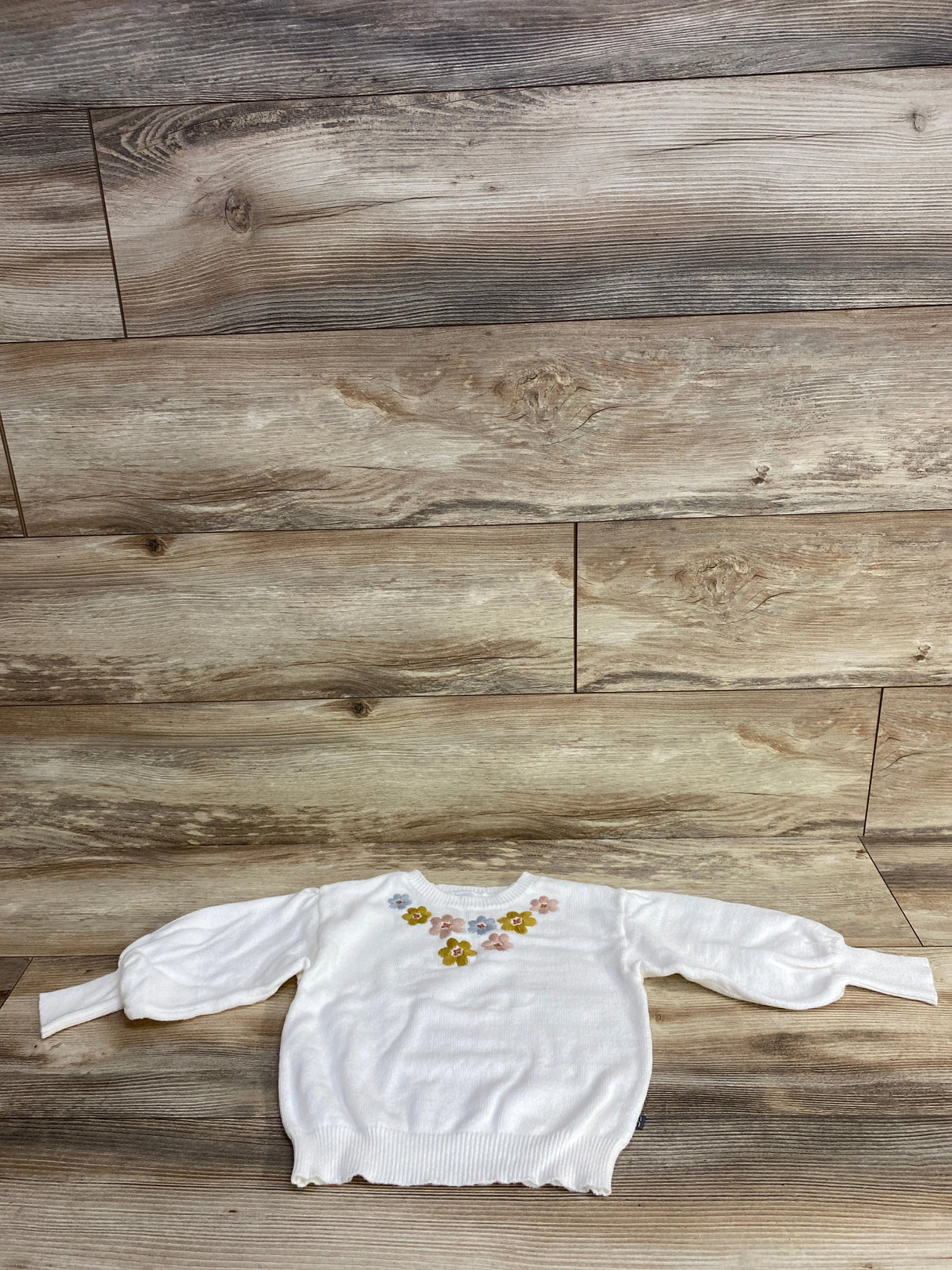 White kids sweater with pastel floral embroidery on chest, long sleeves, knitted fabric on wooden floor