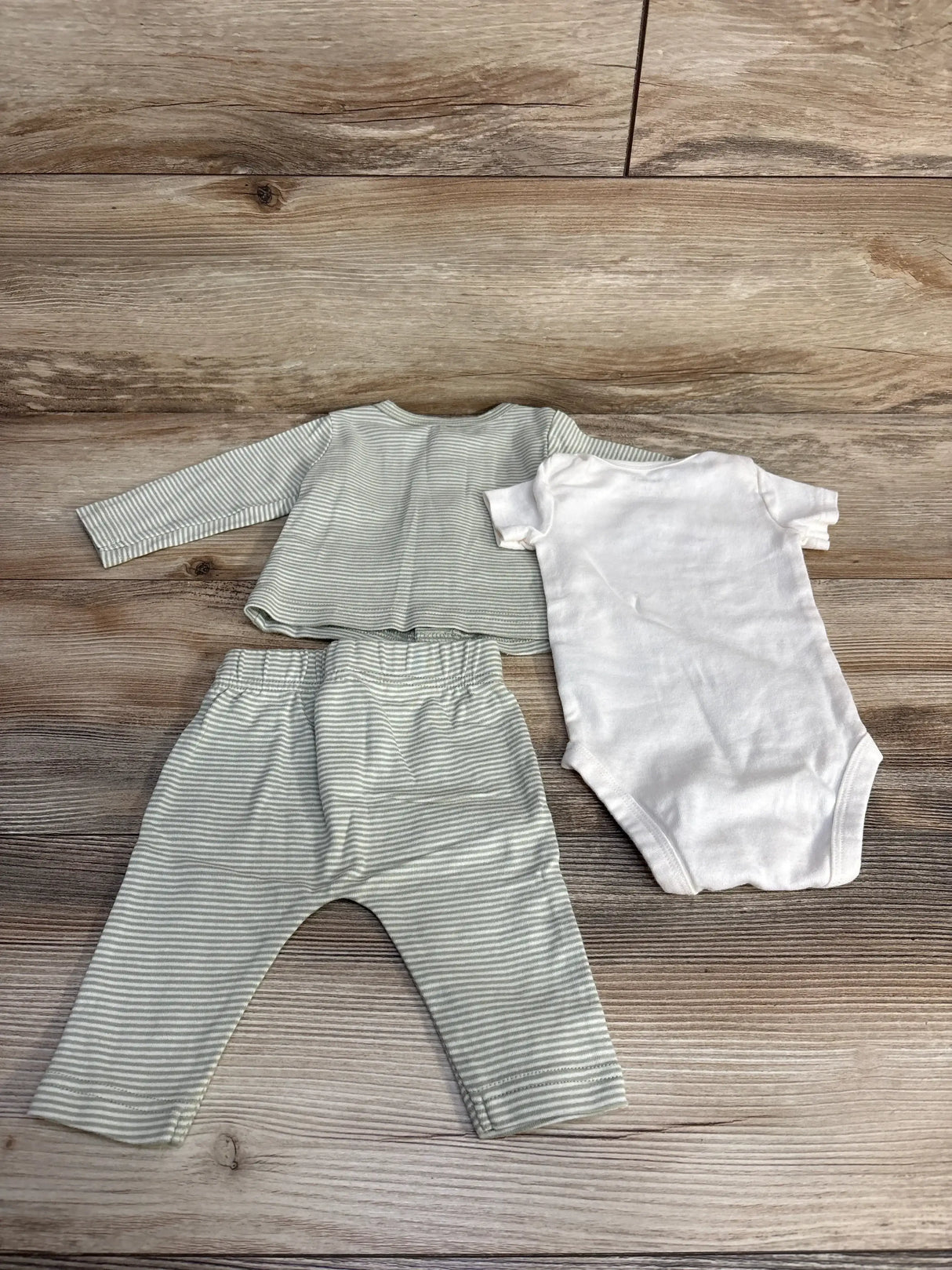 Flat lay of 3-piece Carter’s baby set: white bodysuit with sage-gray striped top and matching striped pants on wood background