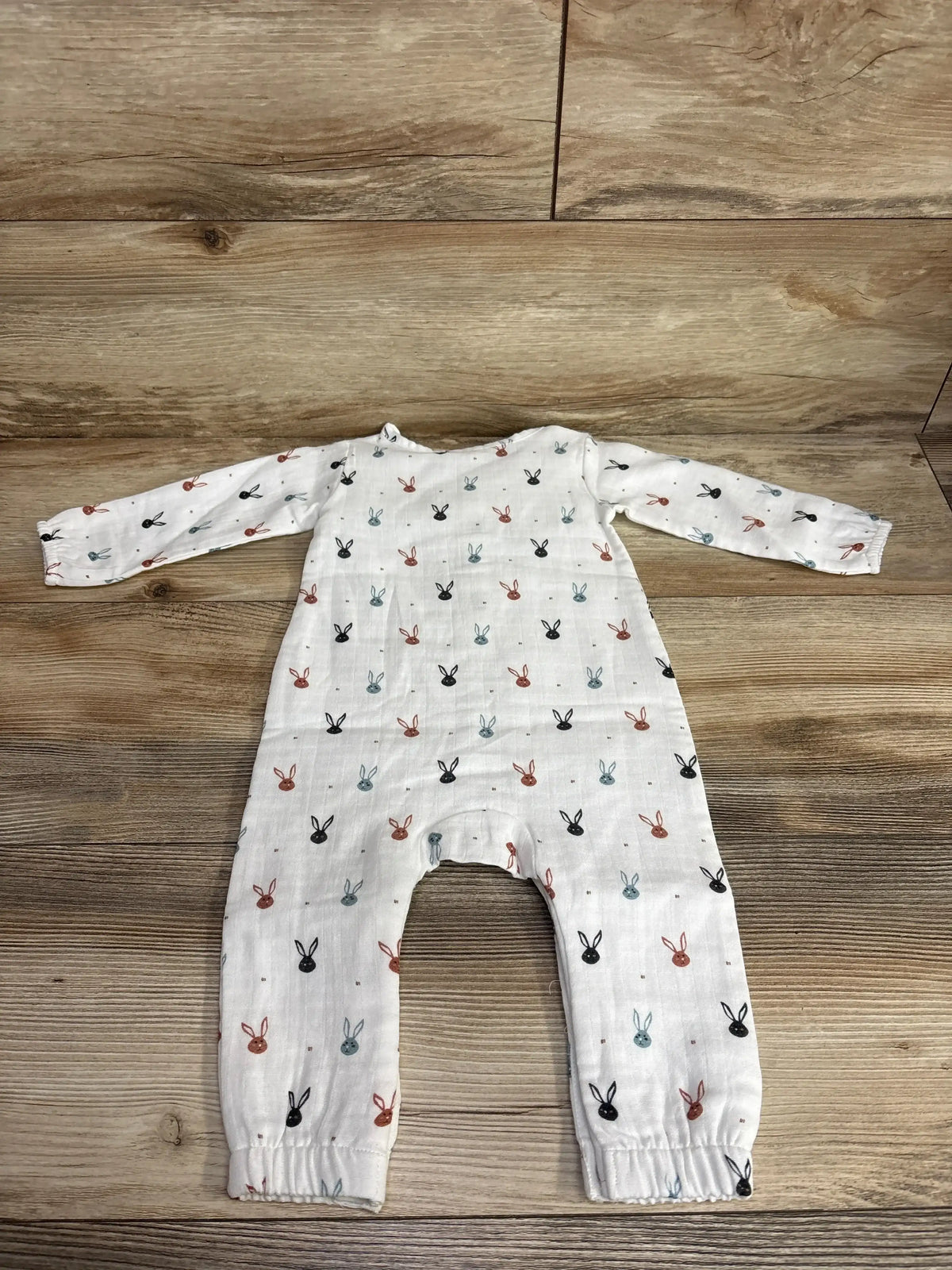 White baby romper with long sleeves and multicolored bunny print on wood background