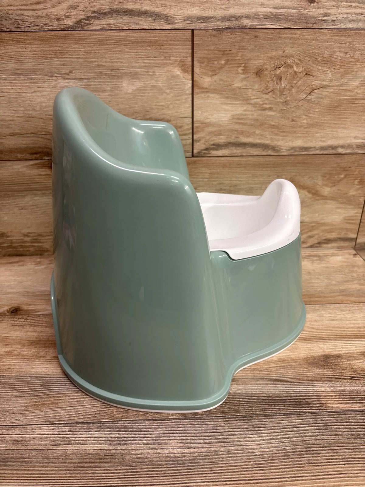 Side view of green BabyBjorn potty chair showcasing its white inner basin against a wood panel background